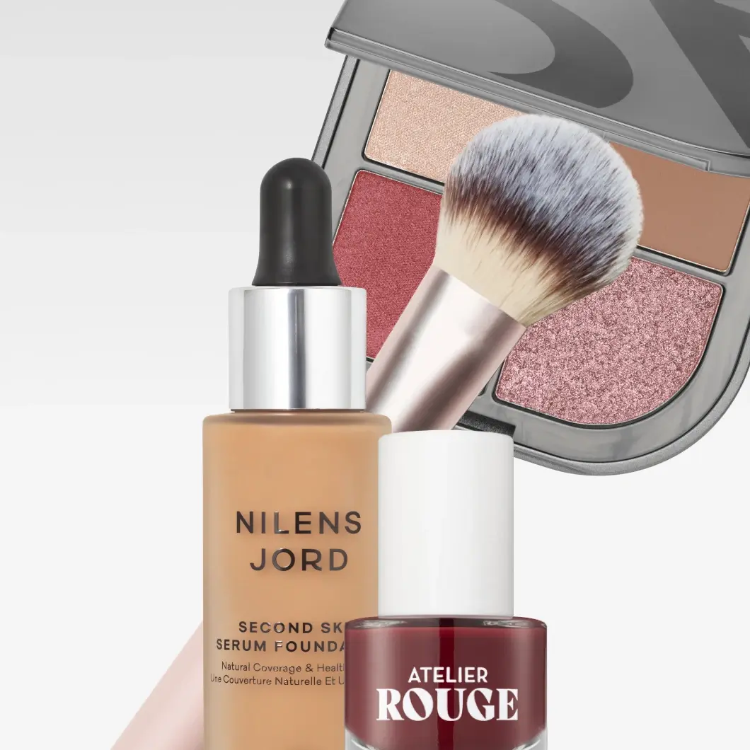 Makeup med Nilens Jord Second Skin Serum Foundation, Natural Coverage & Healthy Glow, en makeupborste, en öppen palett med fyra nyanser i beige, rosa och brunt samt mörkrött Atelier Rouge nagellack.