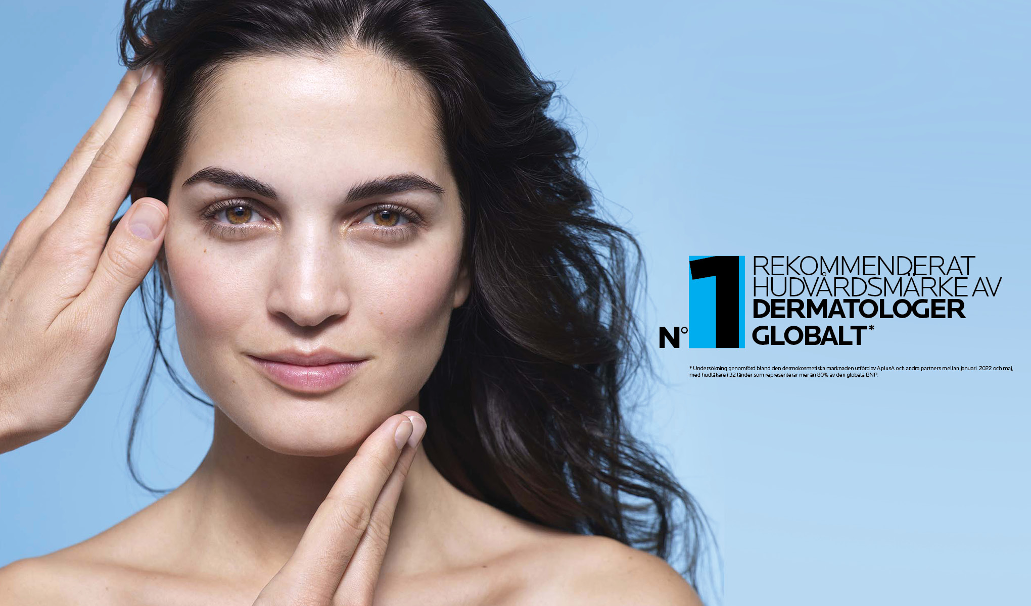 En kvinna med mörkt, vågigt hår mot en ljusblå bakgrund. Texten på bilden lyder "N°1 rekommenderat hudvårdsmärke av dermatologer globalt". Kvinnan håller sina händer nära ansiktet, vilket framhäver hudvårdsbudskapet.