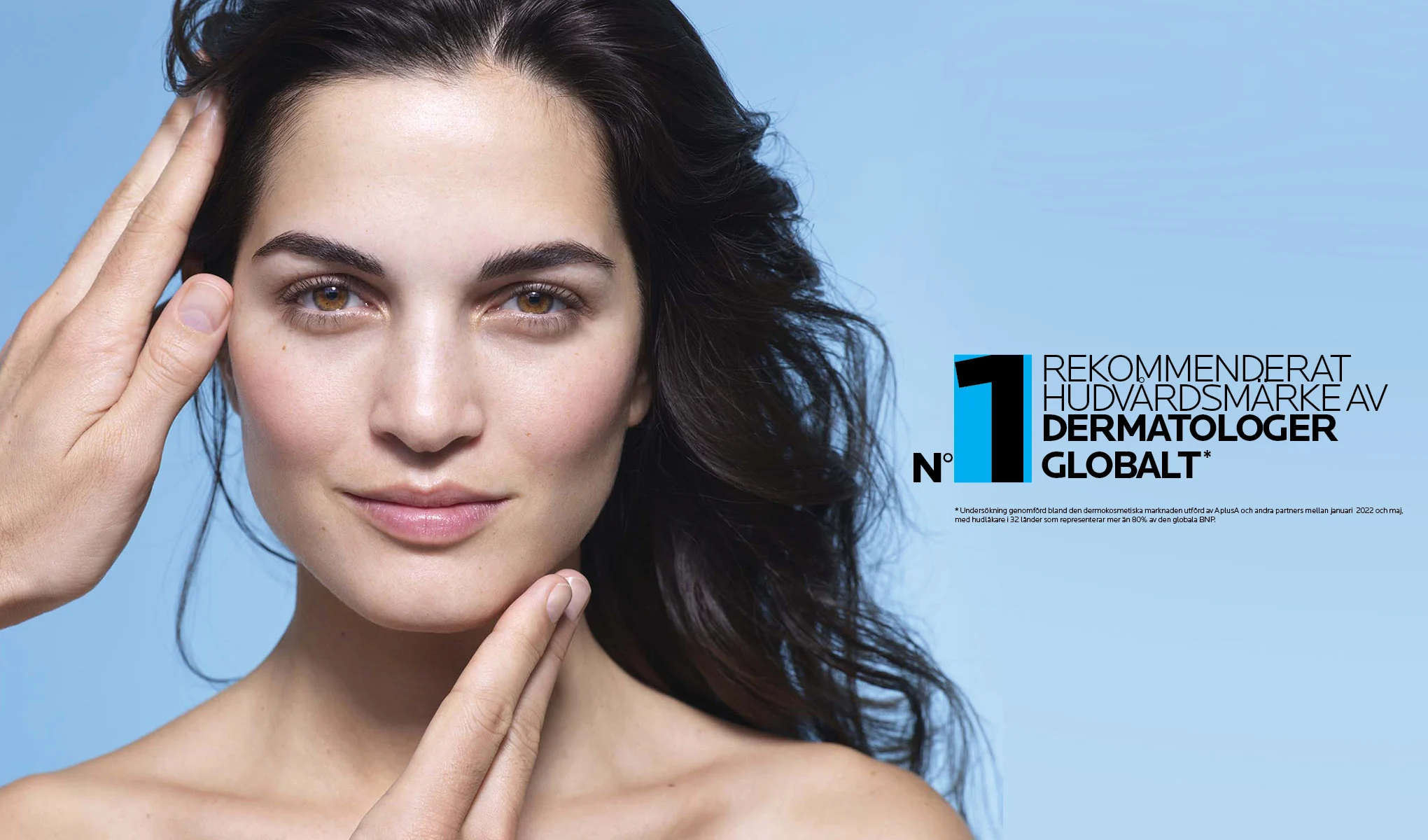 En kvinna med mörkt, vågigt hår mot en ljusblå bakgrund. Texten på bilden lyder "N°1 rekommenderat hudvårdsmärke av dermatologer globalt". Kvinnan håller sina händer nära ansiktet, vilket framhäver hudvårdsbudskapet.