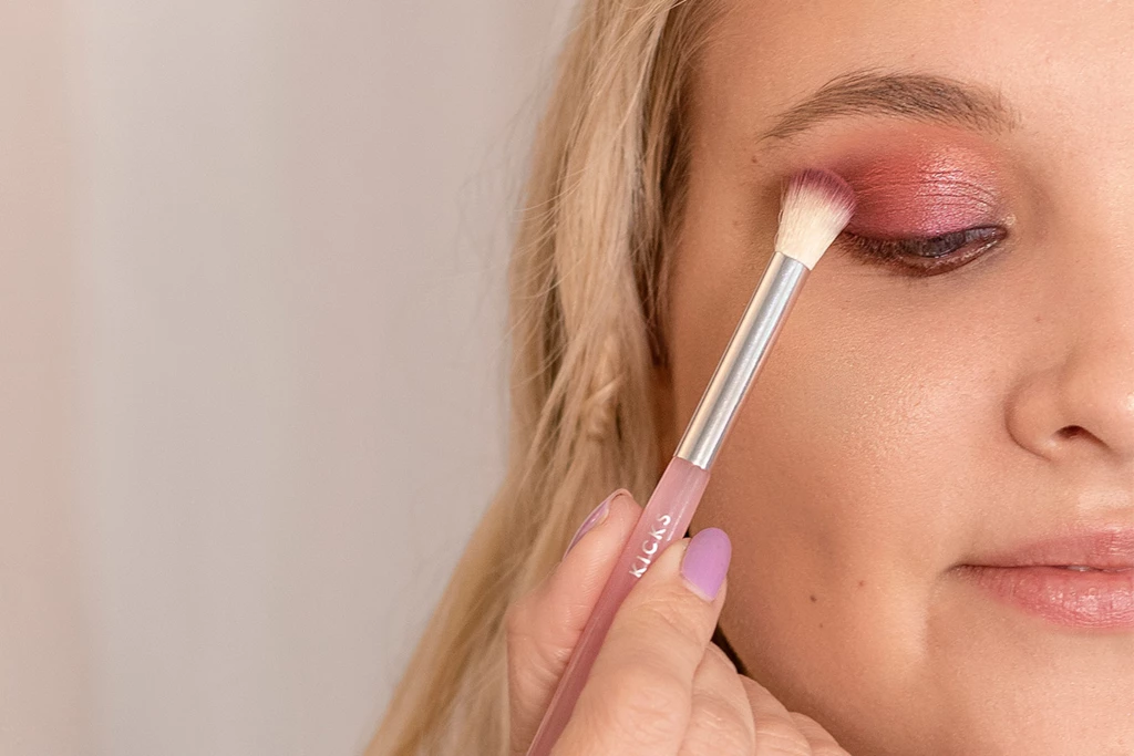 Blond kvinna applicerar skimrande rosa ögonskugga på ögonlocket.