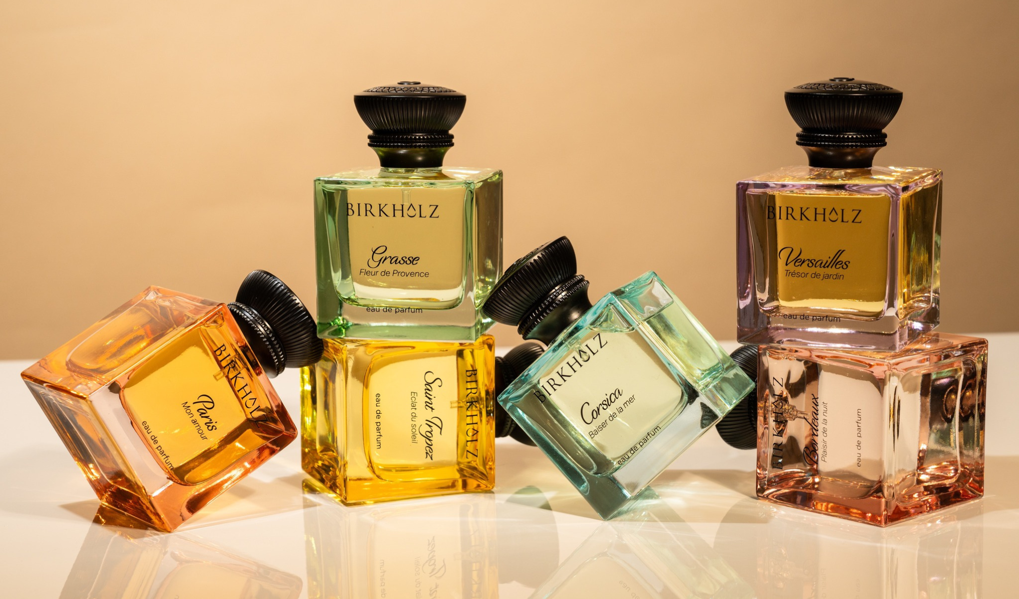 Tuotekuva useista erivärisistä Birkholz eau de parfum -pulloista beigeä taustaa ja peiliheijastusta vasten. Näkyvät tuoksujen nimet ovat “Paris Mon Amour”, “Grasse Fleur de Provence”, “Saint Tropez Éclat du Soleil”, “Corsica Baiser de la mer”, “Versailles Trésor de jardin” ja “Barcelona Pasión de la nuit”.