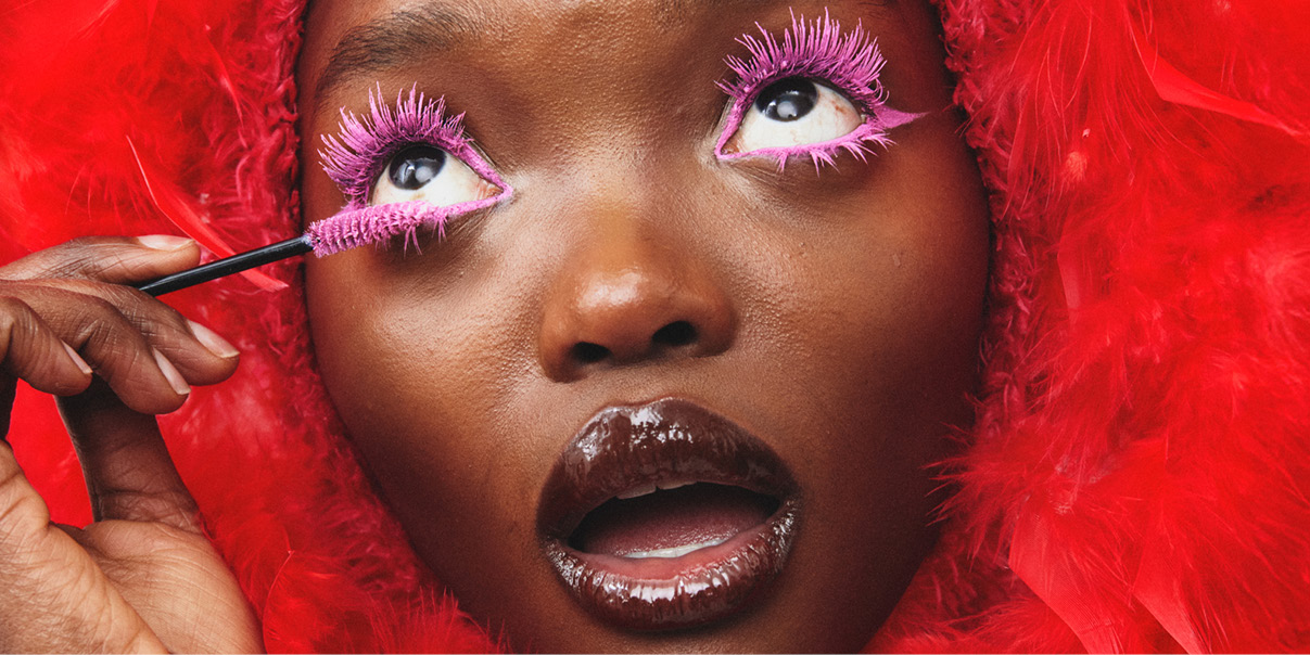 Käsi pitää ohutta sivellintä punaisten höyhenten taustalla.