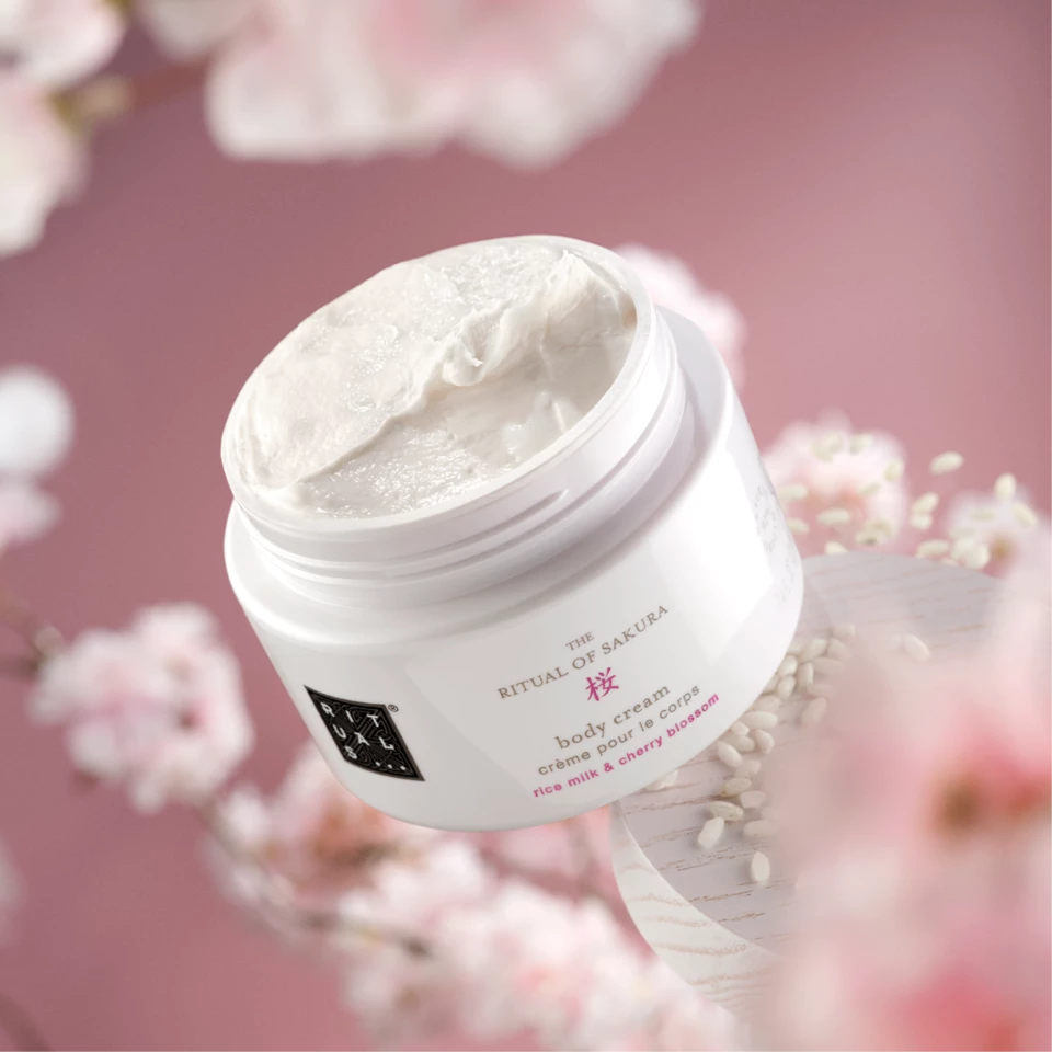 Kroppskrem frå serien «the Rituals of Saktura» med rosa bakgrunn og ei kvist blomstrande kirsebærtre.