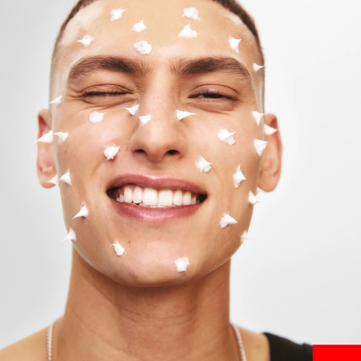 Person med ansiktet täckt av små klickar hudkräm som appliceras jämnt över huden.