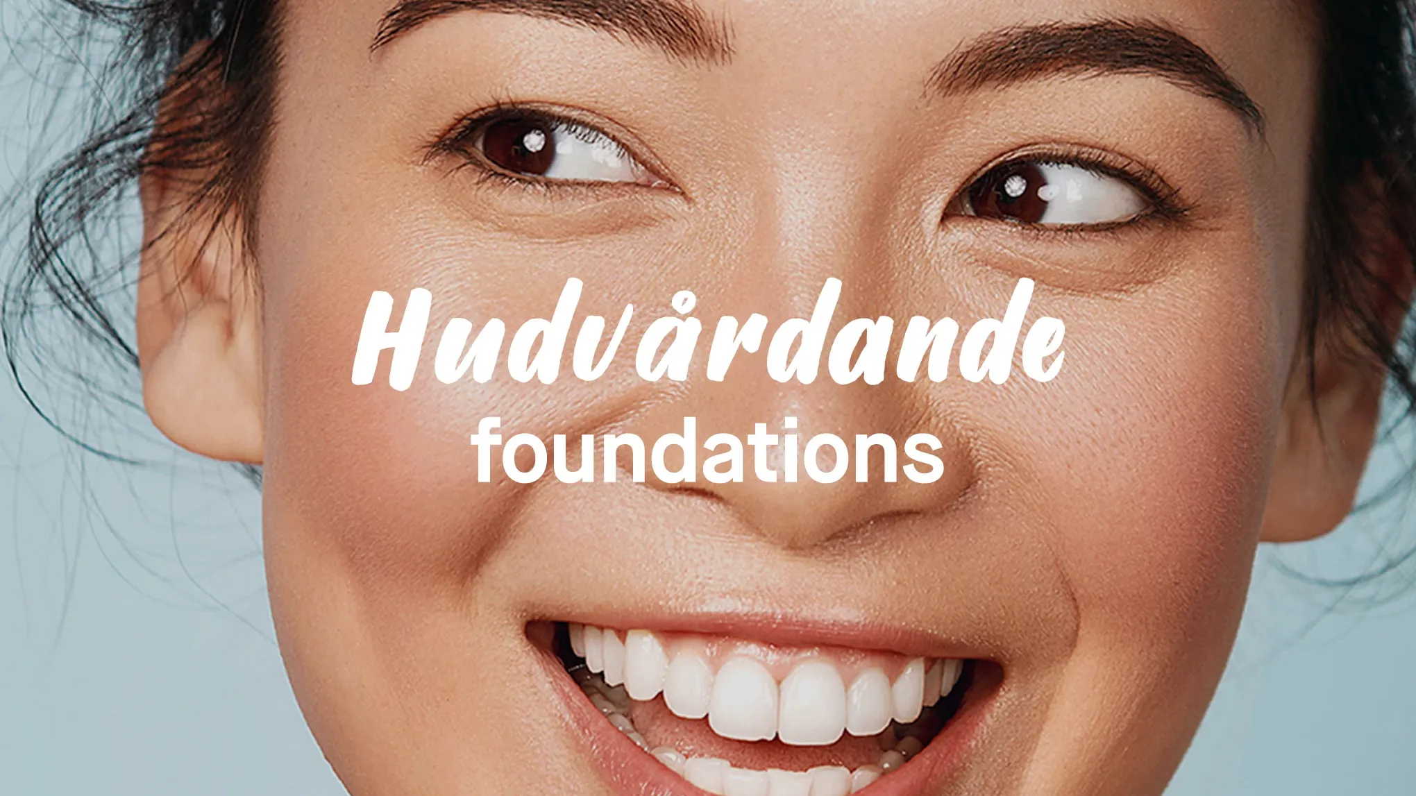 Teksten "Hudpleiende foundations" foran en kvinne med stort smil, mot en grå bakgrunn.