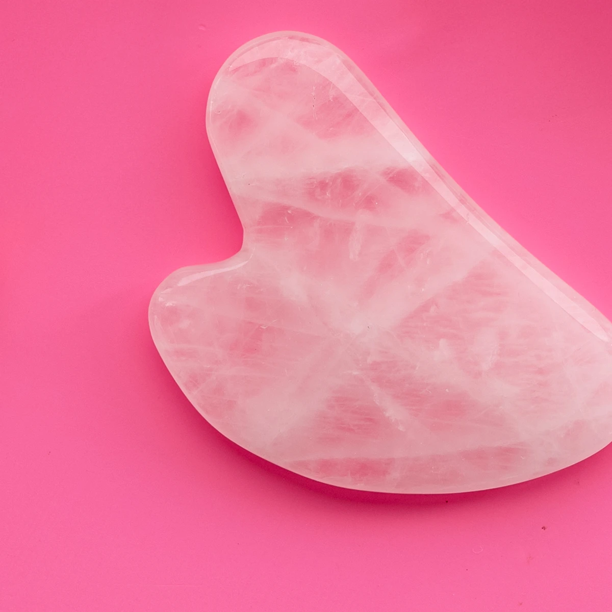 Rosa hjärtformad gua-sha sten mot cerise bakgrund.