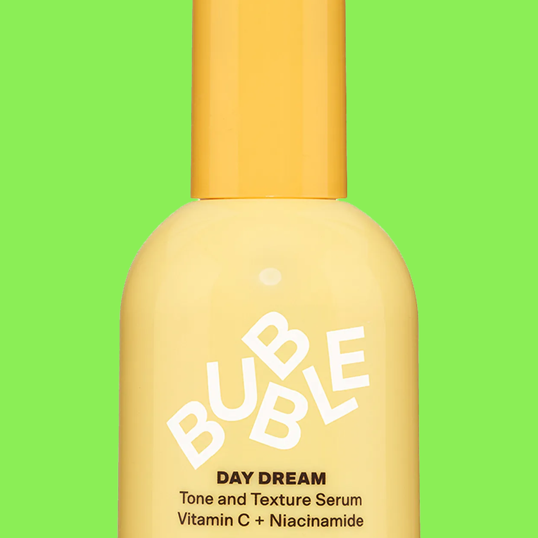 Serumflaska i gul ton med texten “BUBBLE DAY DREAM Tone and Texture Serum Vitamin C + Niacinamide” mot grön bakgrund.