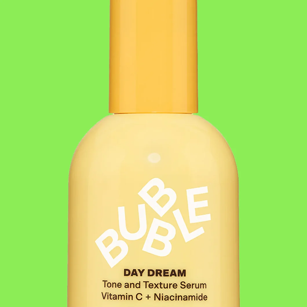 Serumflaska i gul ton med texten “BUBBLE DAY DREAM Tone and Texture Serum Vitamin C + Niacinamide” mot grön bakgrund.