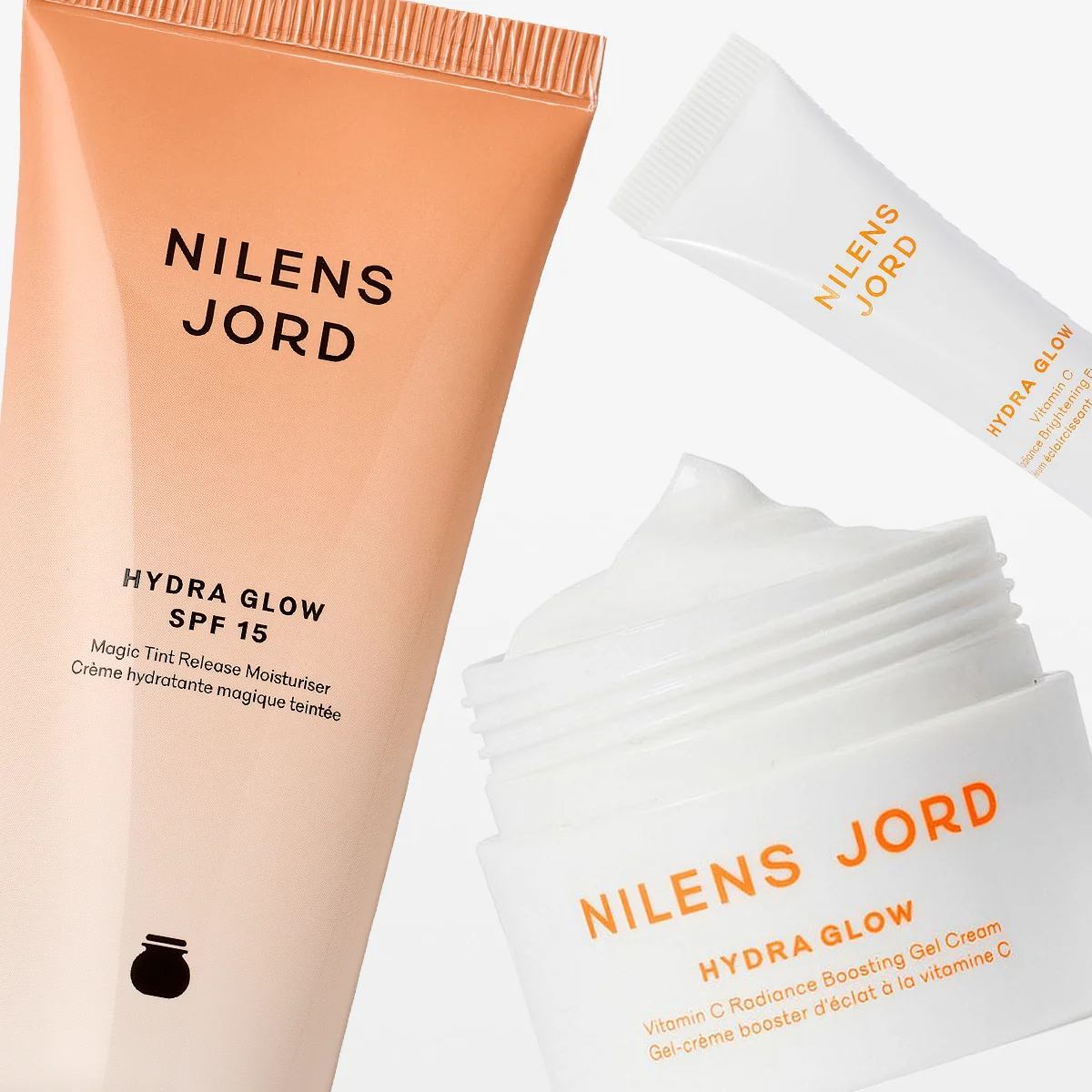 Tre hudvårdsprodukter från Nilens Jord ur serien Hydra Glow visas mot en ljus bakgrund. Bilden inkluderar en fuktgivande dagkräm med SPF 15, en gelkräm i burk och en ögonkräm. Produkterna har en beige till vit design och förmedlar en känsla av återfuktning, lyster och naturlig skönhet.