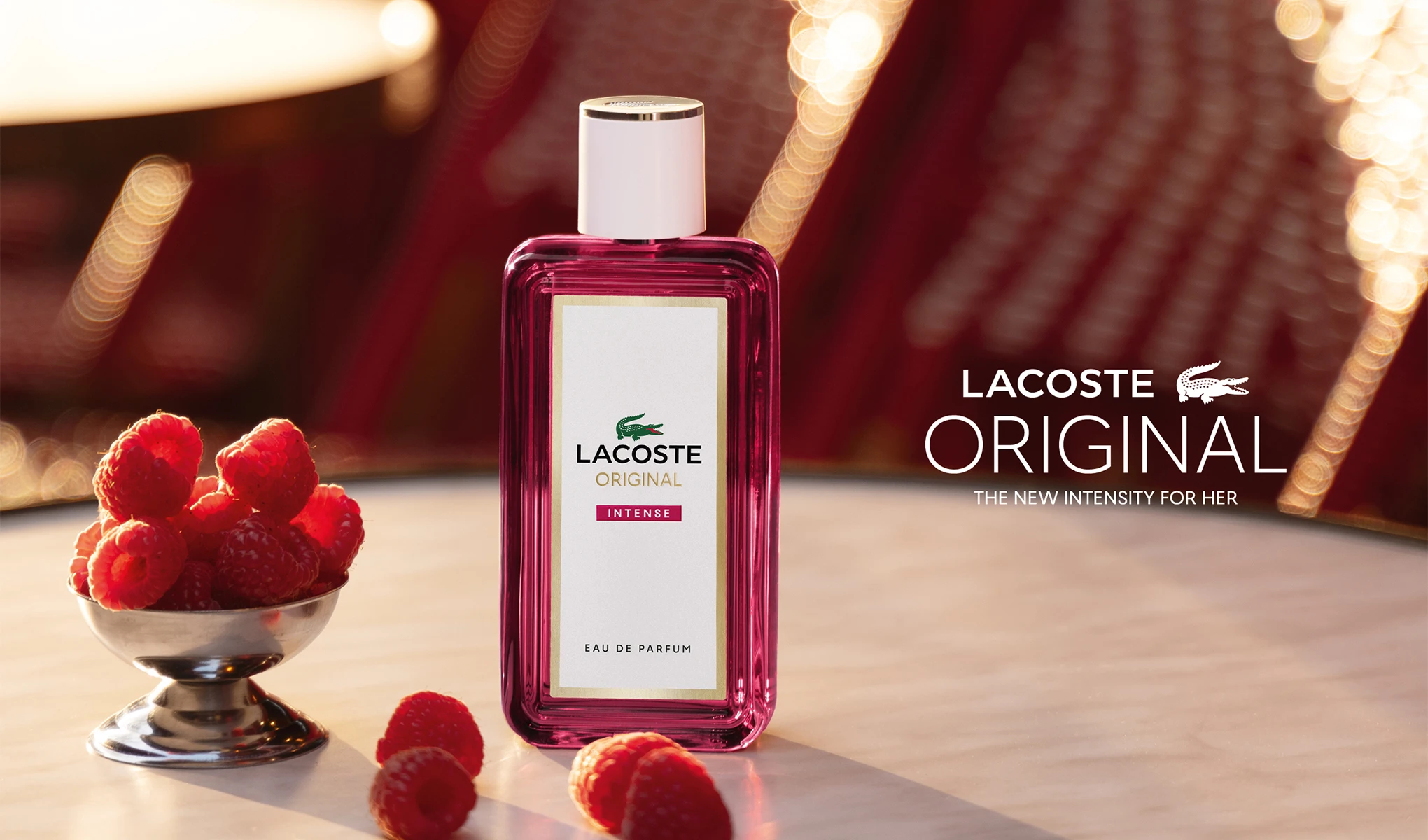 Lacoste Original Intense-parfymeflaske ved siden av bringebær. Tekst: «Lacoste Original. The new intensity for her.»