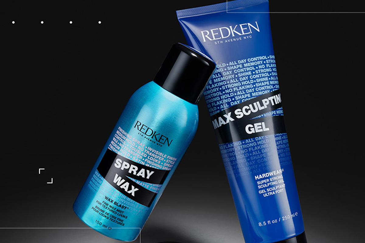 To hårpleieprodukter fra Redken står mot en mørk bakgrunn. Det ene produktet er en blå sprayflaske, og det andre er en blå tube. Produktene er plassert slik at de lener seg mot hverandre.