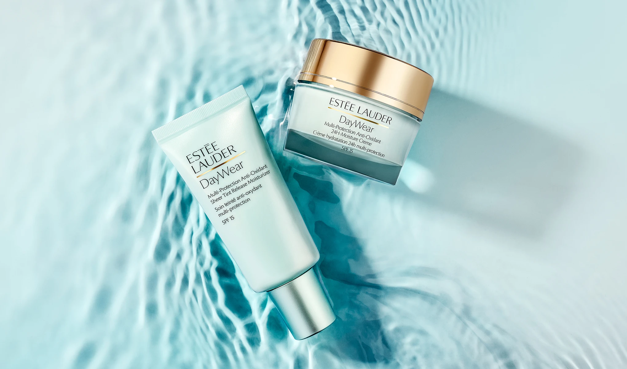 Kaksi Estée Lauder DayWear -ihonhoitotuotetta on aseteltu vaaleansiniselle veden pinnalle, jossa näkyy valon heijastuksia. Kuvassa on tuubi, jossa lukee ”ESTÉE LAUDER DayWear Multi-Protection Anti-Oxidant Sheer Tint Release Moisturizer SPF 15”, sekä purkki, jossa lukee ”ESTÉE LAUDER DayWear Multi-Protection Anti-Oxidant 24H-Moisture Creme SPF 15”.