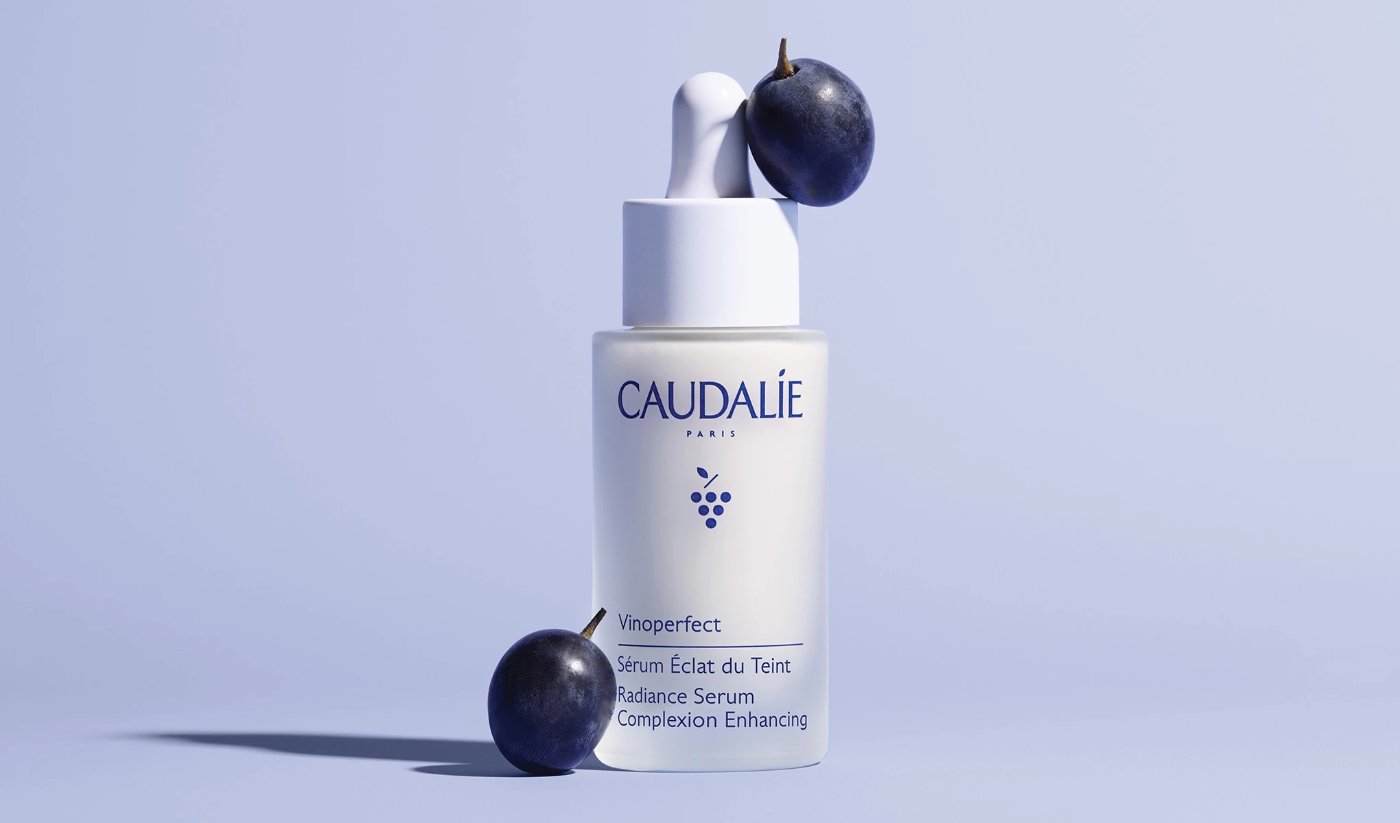Produktet Vinoperfect fra Caudalie sammen med et par druer mot en blå bakgrunn.