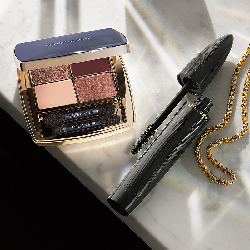 Estée Lauder -luomiväripaletti ja ripsiväri marmoripinnalla kultaketjun kanssa.