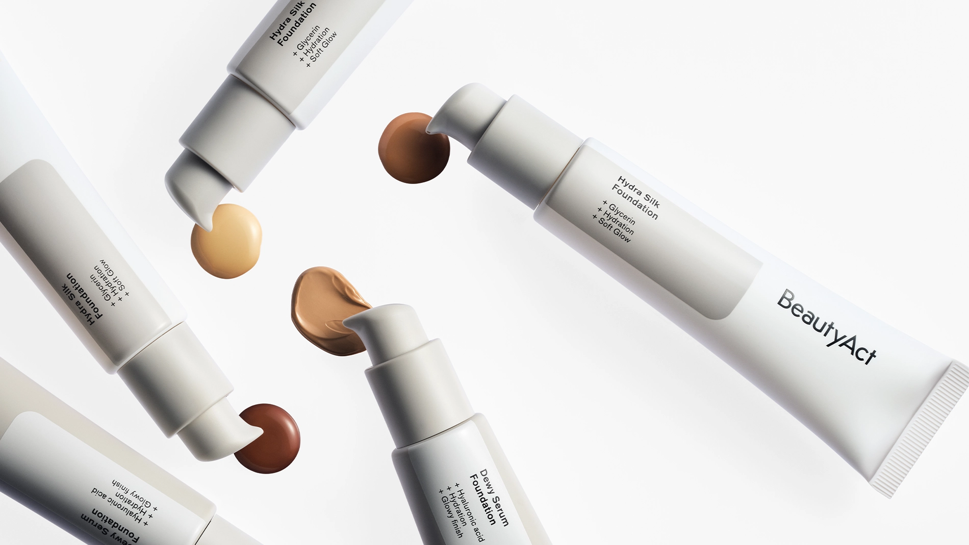 Bilde som viser forskjellige foundationprodukter fra BeautyAct. På bildet vises fem tuber med forskjellige nyanser av foundation, inkludert lys, medium og mørk. Hver tube har en pumpe som slipper ut en liten mengde foundation. Produktene er arrangert i en sirkel på en hvit bakgrunn.