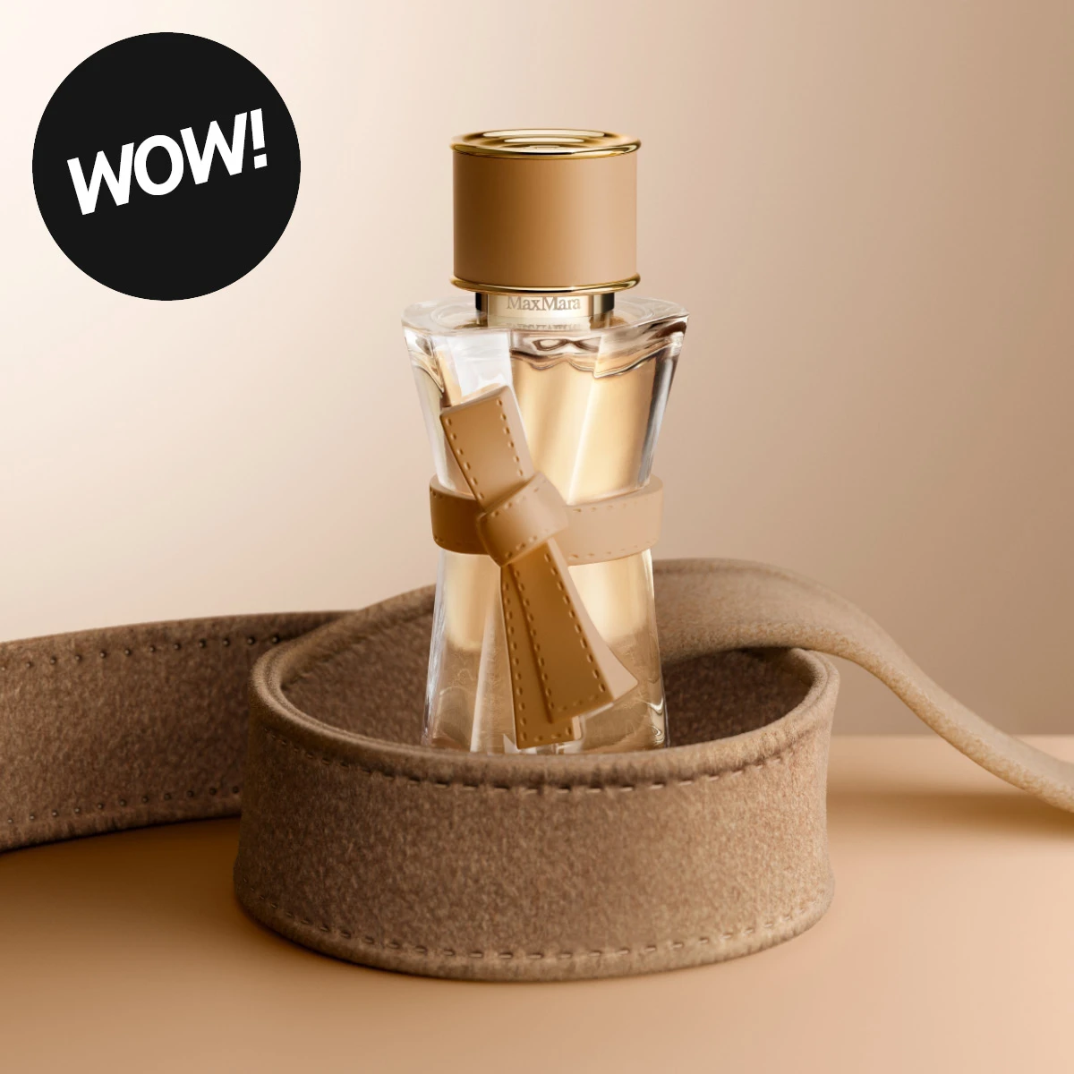 Max Mara parfym i en transparent glasflaska med guldfärgad kork och beige rosettdetalj runt flaskan. Parfymen står i en rund beige filtdekoration mot en ljus bakgrund, med texten ”WOW!” i en svart cirkel.
