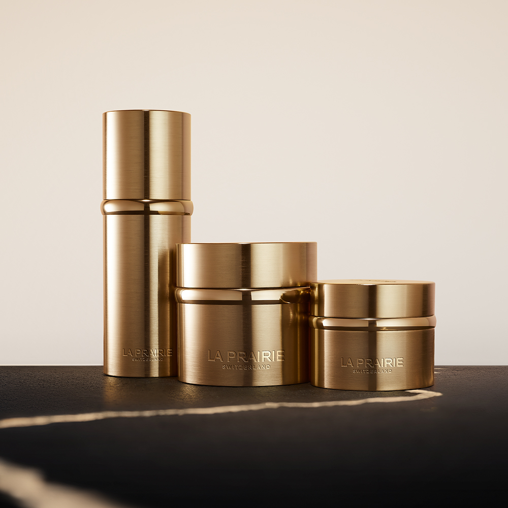 La Prairie Pure Gold -ihonhoitotuotteet kultaisissa purkeissa ja pullossa, aseteltuna hillitylle, vaalealle taustalle.