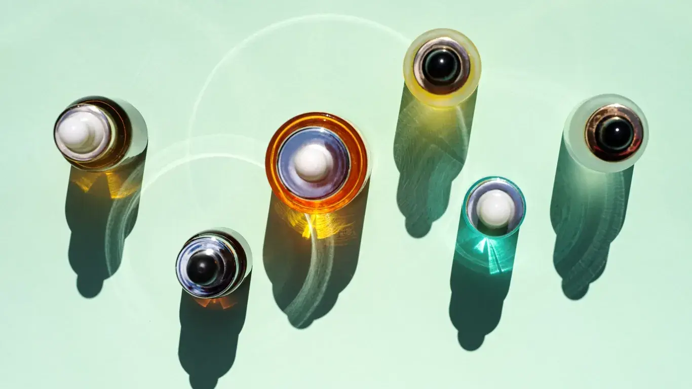 Färgglada droppflaskor för hudvård kastar skuggor på en grön bakgrund.