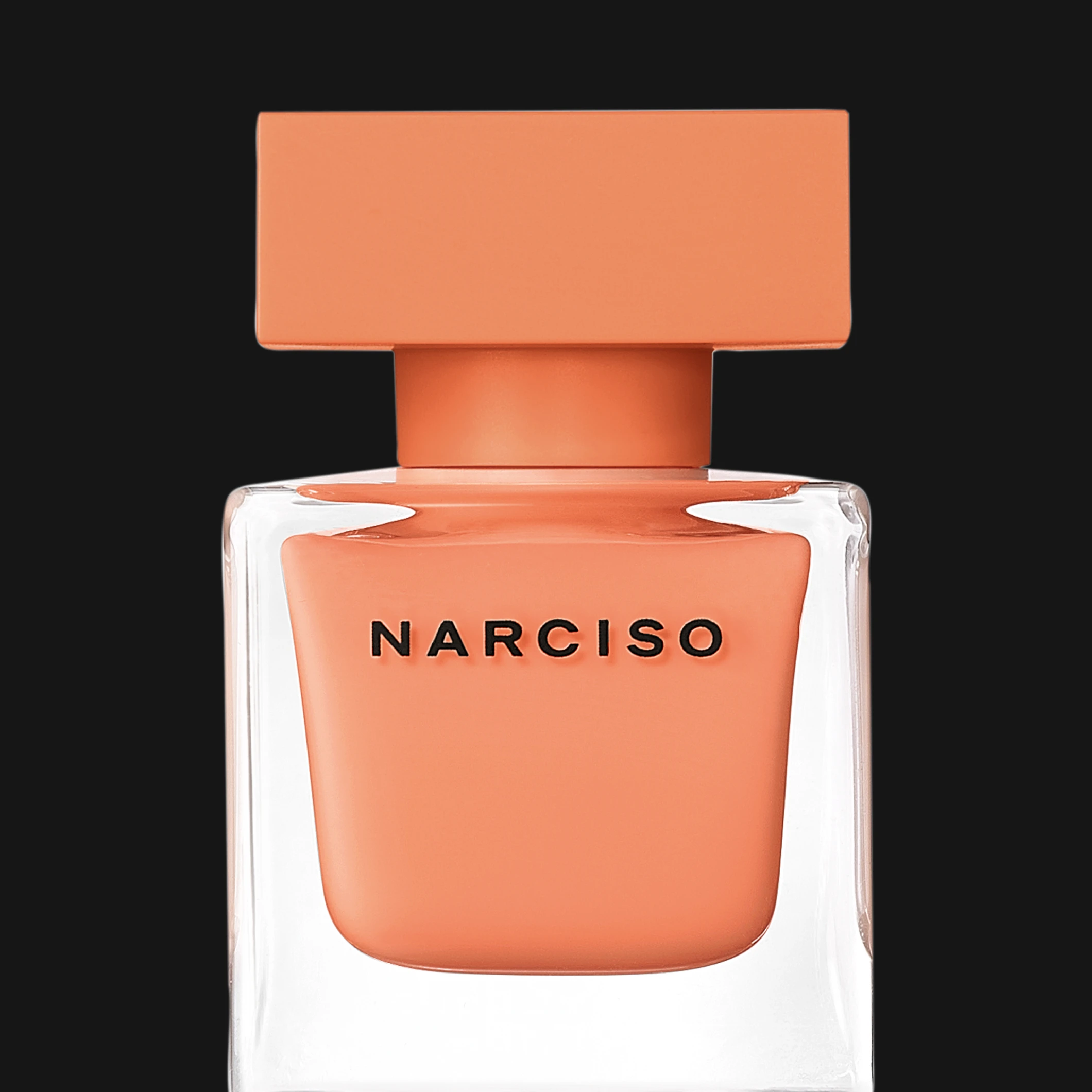 Narciso parfymflaska i transparent glasdesign med korallfärgad innerflaska och matchande kork mot svart bakgrund. Synlig text inkluderar “NARCISO”.