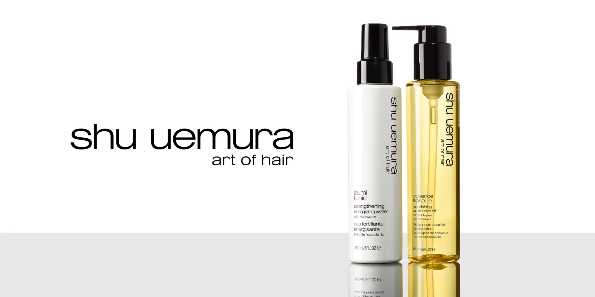 En vit flaska Izumi Tonic och en genomskinlig gul flaska Essence Absolue, båda med svarta pumpar, mot en vit bakgrund med reflektion på en blank yta.