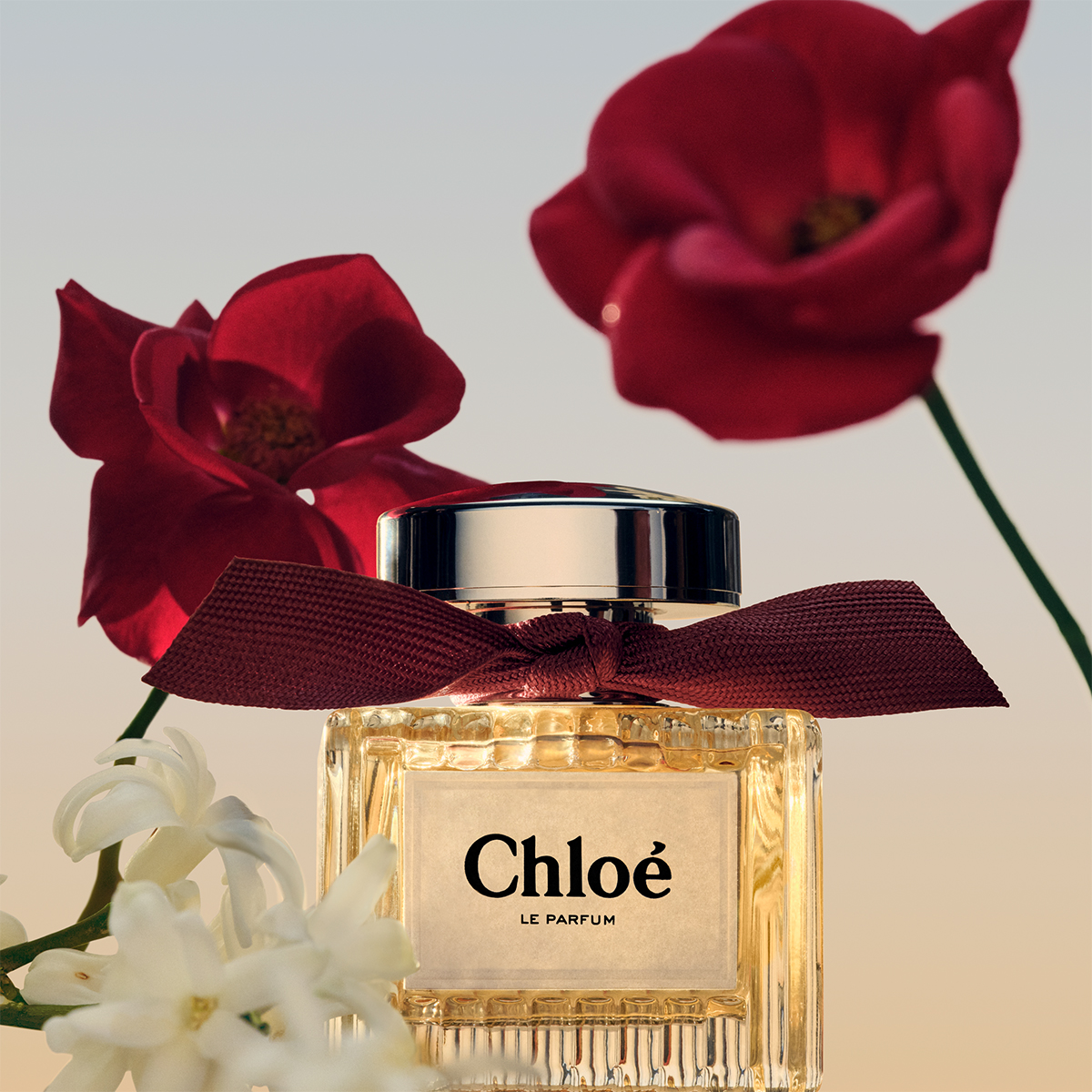 Chloé Le Parfum - Parfymeflaske med vinrød sløyfe. Bakgrunnen har røde og hvite blomster.