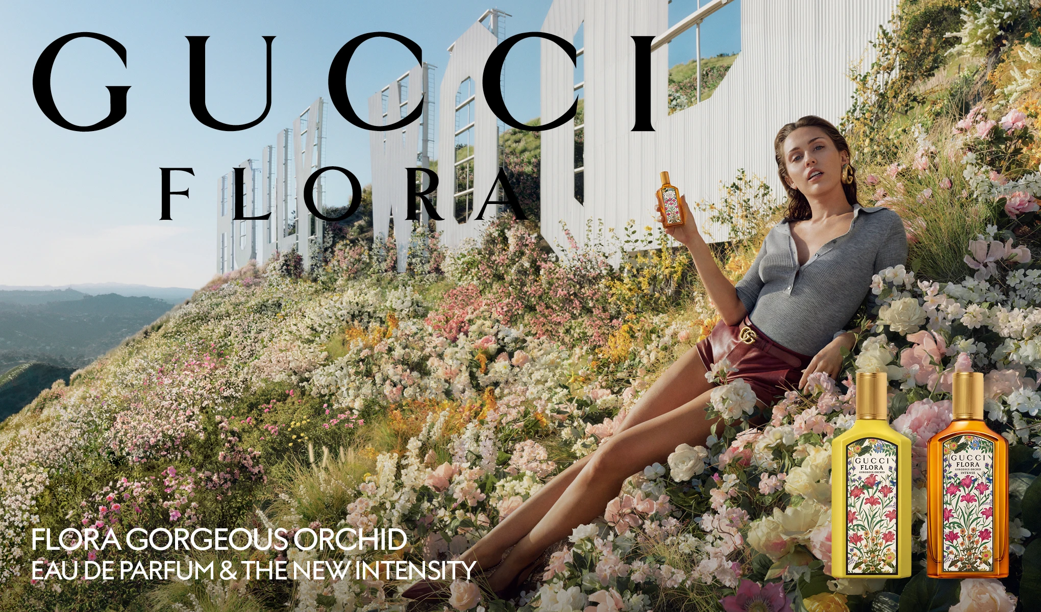 Henkilö istuu kukkien keskellä valkoisen Hollywood-kyltin edessä ja pitelee Gucci Flora -hajuvesipulloa. Yläosassa näkyy teksti "GUCCI FLORA" ja alaosassa teksti "FLORA GORGEOUS ORCHID EAU DE PARFUM & THE NEW INTENSITY". Oikeassa alakulmassa näkyvät hajuvesipullot etiketeillä "GUCCI FLORA GORGEOUS ORCHID" ja "GUCCI FLORA GORGEOUS ORCHID INTENSE".