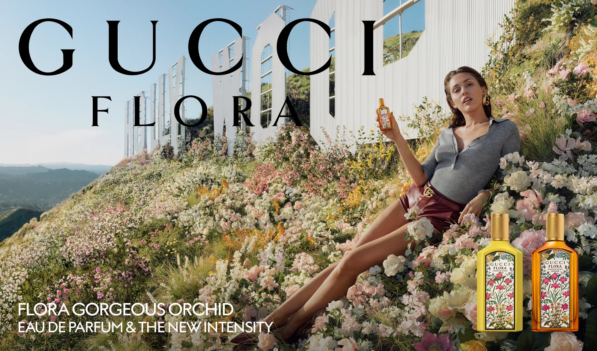 Henkilö istuu kukkien keskellä valkoisen Hollywood-kyltin edessä ja pitelee Gucci Flora -hajuvesipulloa. Yläosassa näkyy teksti "GUCCI FLORA" ja alaosassa teksti "FLORA GORGEOUS ORCHID EAU DE PARFUM & THE NEW INTENSITY". Oikeassa alakulmassa näkyvät hajuvesipullot etiketeillä "GUCCI FLORA GORGEOUS ORCHID" ja "GUCCI FLORA GORGEOUS ORCHID INTENSE".