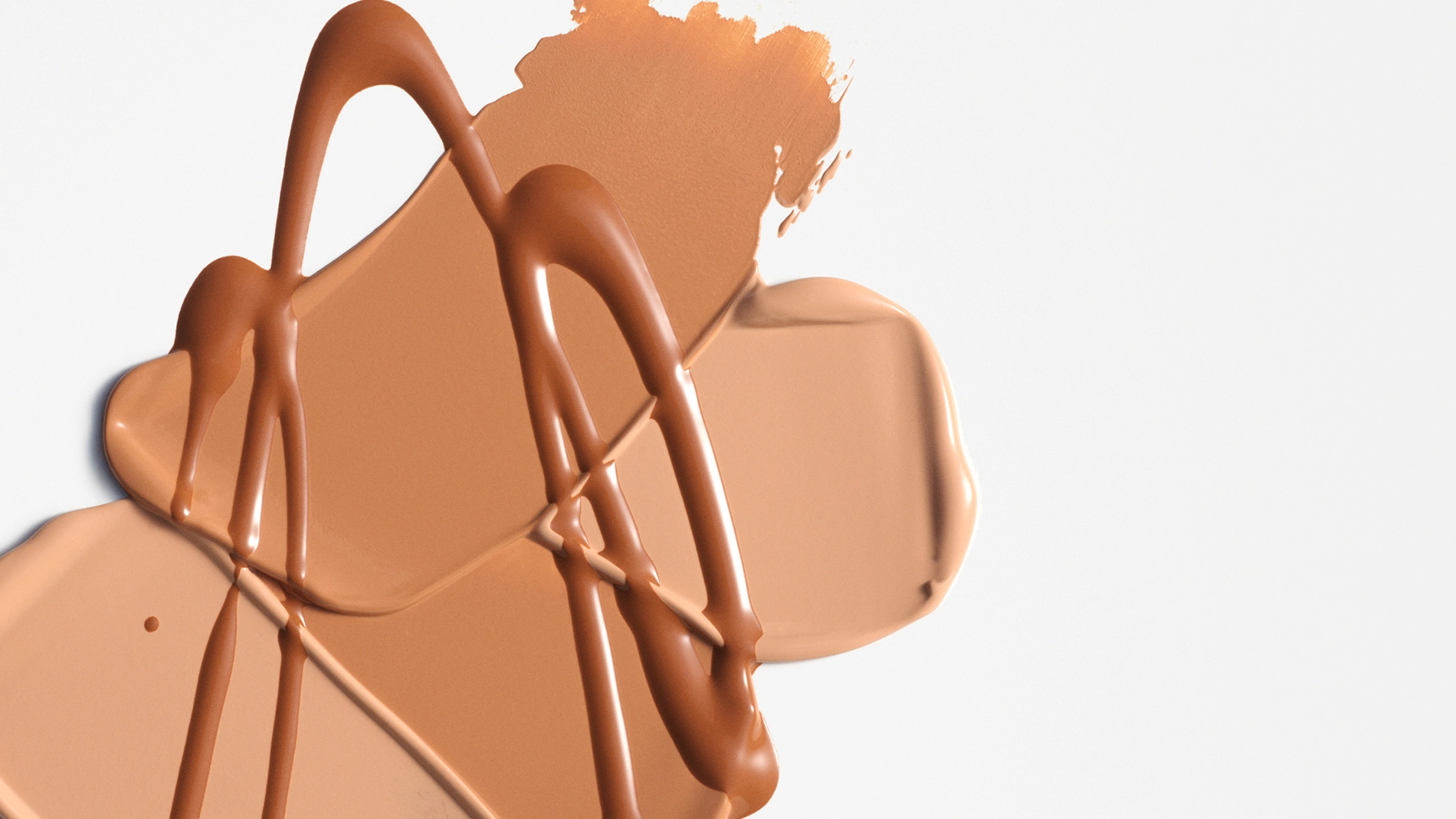 Nærbilde av kremet foundation eller concealer i beige nyanse smurt ut i brede strøk med blanke dråper oppå mot lys bakgrunn. Flytende makeup i nøytral tone med synlig tekstur og dekkende finish.