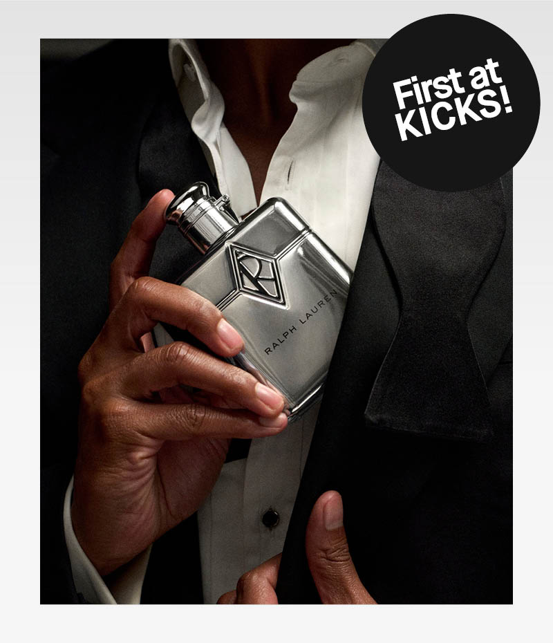 Lähikuva henkilöstä puvussa pitelemässä Ralph Lauren -hajuvettä. Mustassa tarrassa lukee ”First at KICKS!”.