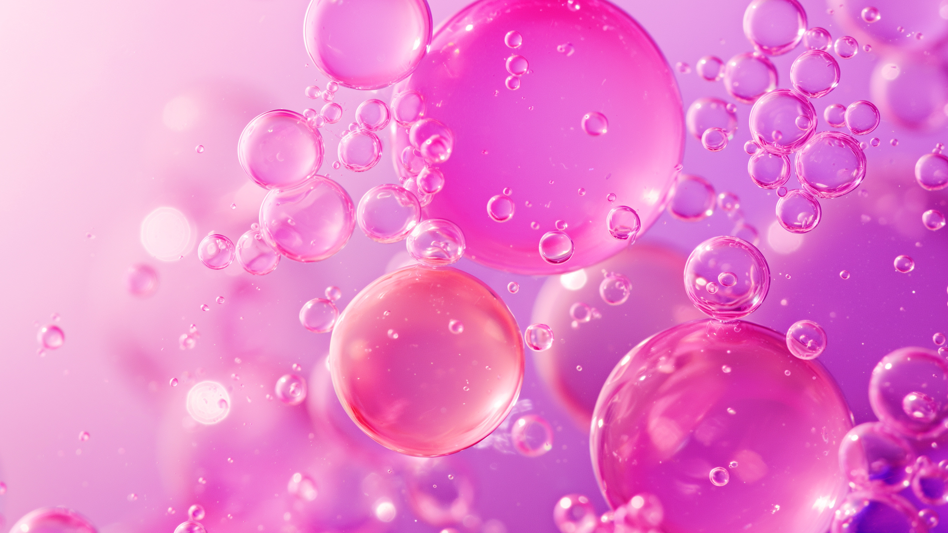 Vaaleanpunaisia ja violetteja läpikuultavia kuplia kelluu pehmeällä violetilla taustalla.