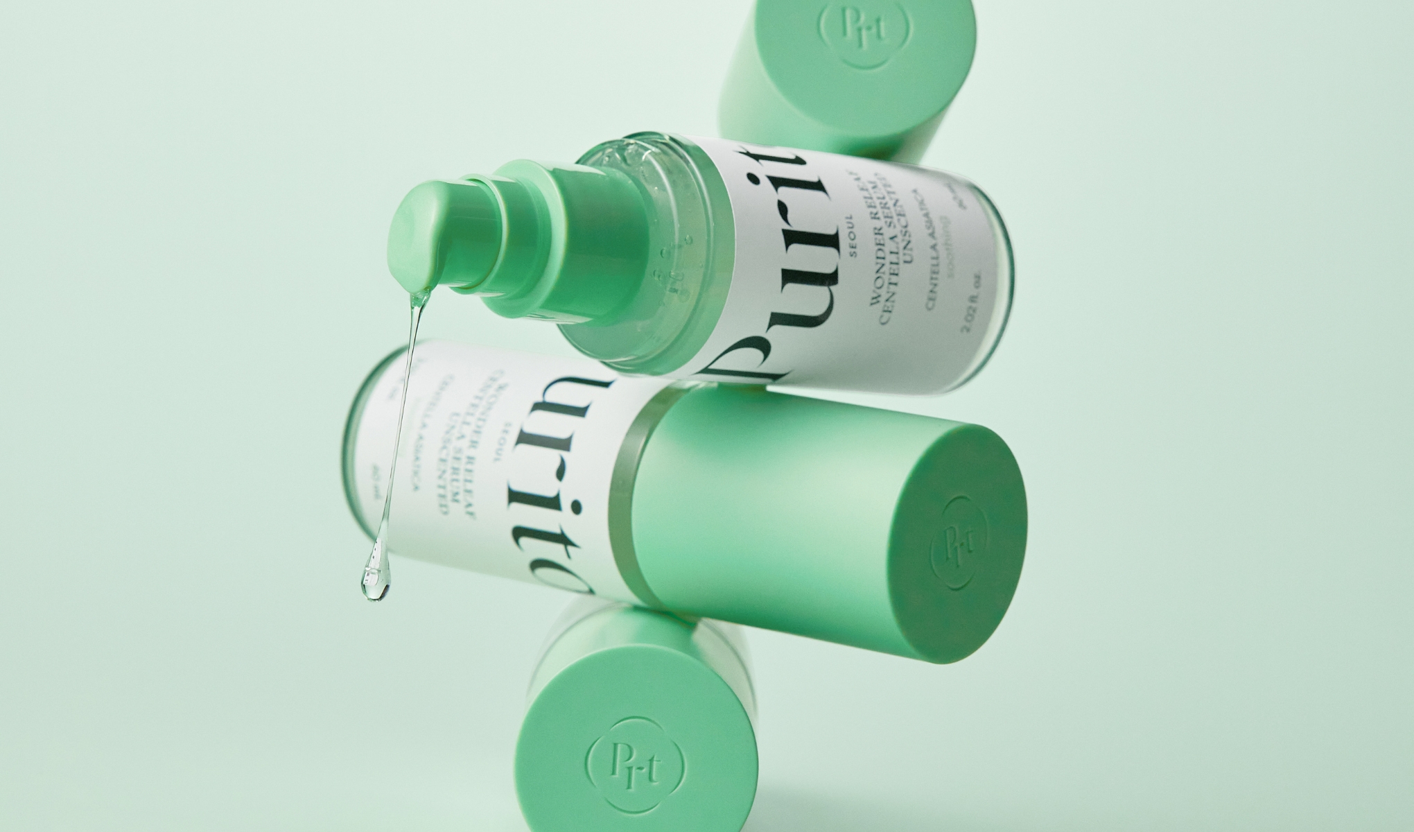 Närbild på en grön Purito-serumflaska med en droppe som rinner ut, med mintgröna lock i bakgrunden.