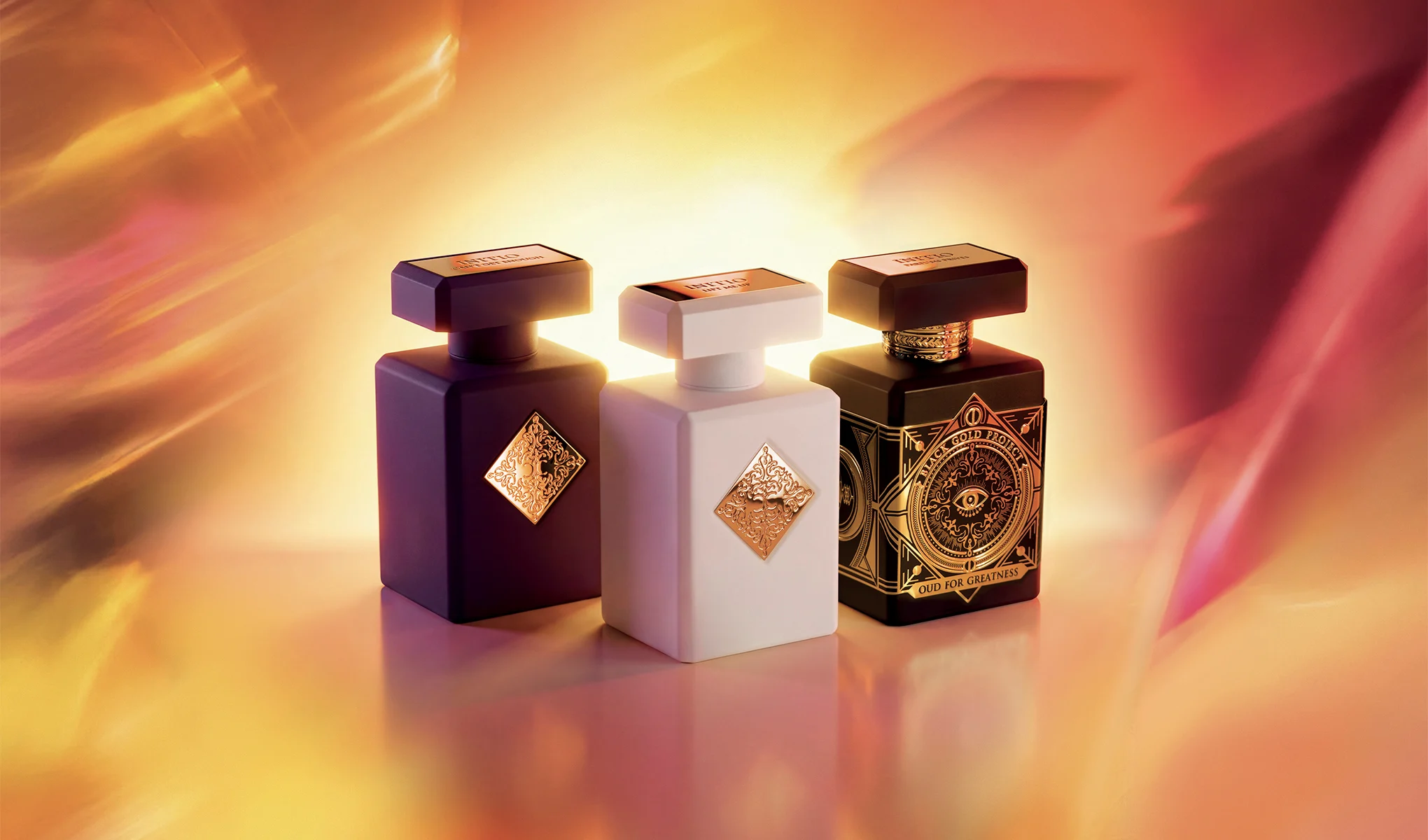 Tre Initio Parfums Privés-parfymeflasker mot en varm, gyllen bakgrunn.