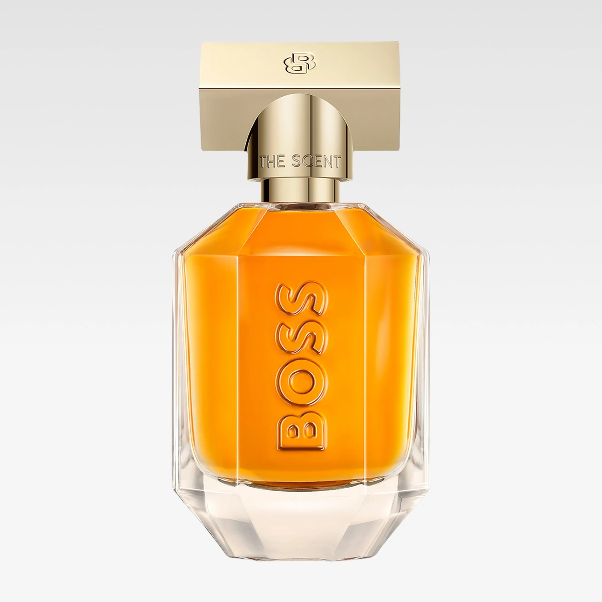 Hugo Boss The Scent-parfymeflaske med gyllen kork og oransje parfyme mot lys grå bakgrunn. Synlig tekst inkluderer “THE SCENT” og “BOSS”.