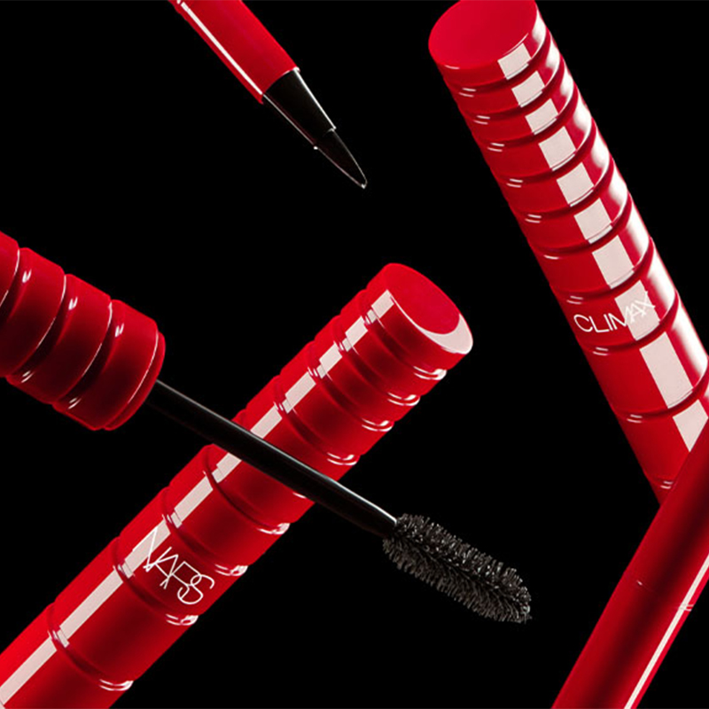Useita NARS-meikkituotteita, kuten ripsiväriä ja eyelineria, mustaa taustaa vasten. Tuotteissa on punaiset kotelot, joihin on painettu NARS-logo valkoisella. Ripsiväriharja ja eyeliner-kynä ovat näkyvissä.