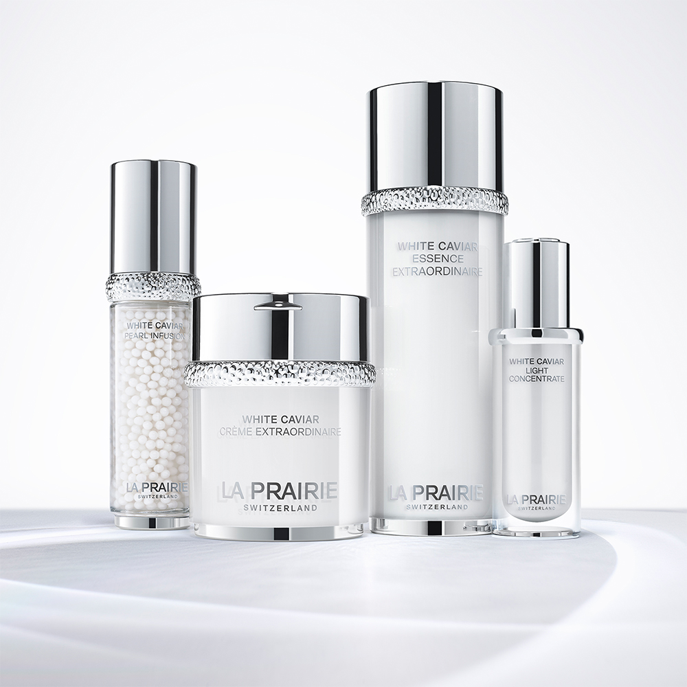 La Prairie White Caviar -ihonhoitotuotteet hopeanvalkoisissa pulloissa ja purkissa, aseteltuna kirkkaalle ja vaalealle alustalle.