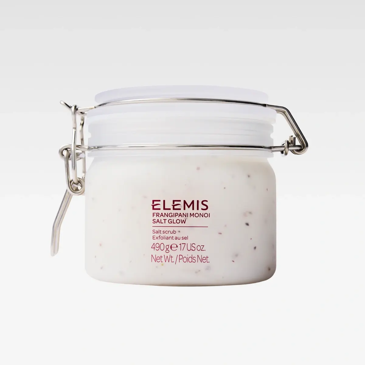 Krukke med kroppsskrubb fra ELEMIS med teksten “ELEMIS Frangipani Monoi Salt Glow”, “Salt scrub”, “Exfoliant au sel”, “490 g e 17 US oz.” og “Net Wt./Poids Net.”. Hvit eksfolierende saltskrubb med små korn i en glasskrukke med metallklemme.