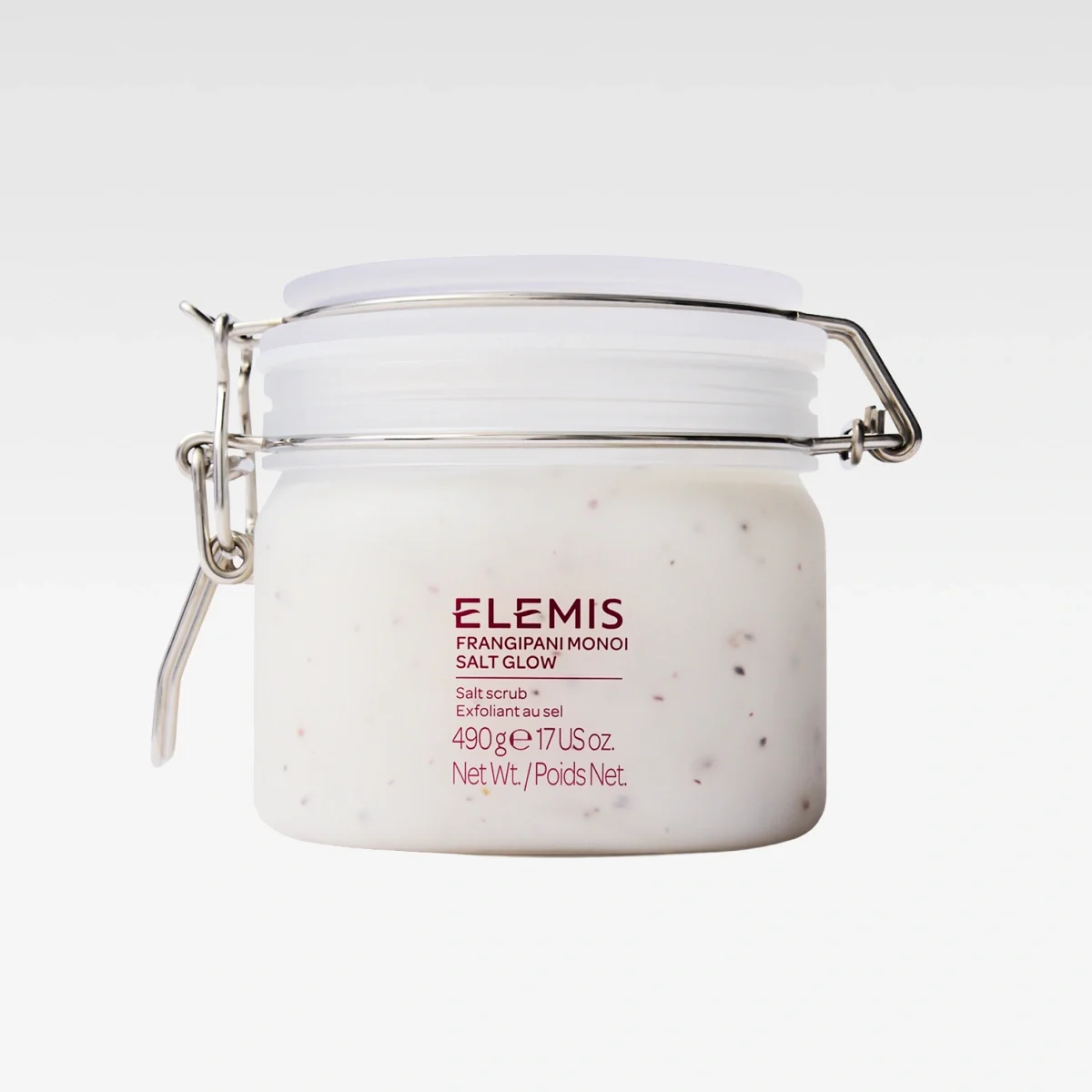 Burk med kroppsskrubb från ELEMIS med texten “ELEMIS Frangipani Monoi Salt Glow”, “Salt scrub”, “Exfoliant au sel”, “490 g e 17 US oz.” och “Net Wt./Poids Net.”. Vit exfolierande salt scrub med små korn i en glasburk med metallspänne.