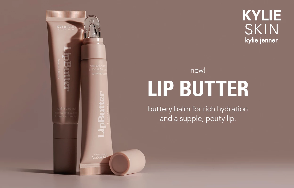 Kylie Skinin Lip Butter yhdessä tekstin "new! LIP BUTTER buttery balm for rich hydration and a supple, pouty lip." kanssa ruskeaa taustaa vasten.