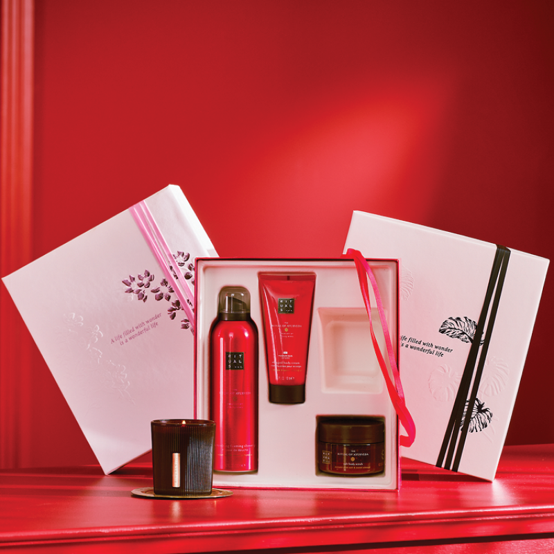 Rituals presentset som innehåller duschgel, kroppskräm och skrubbkräm i en röd förpackning, samt ett svart ljus. Presentförpackningen är vit och dekorerad med rosa och svart band.