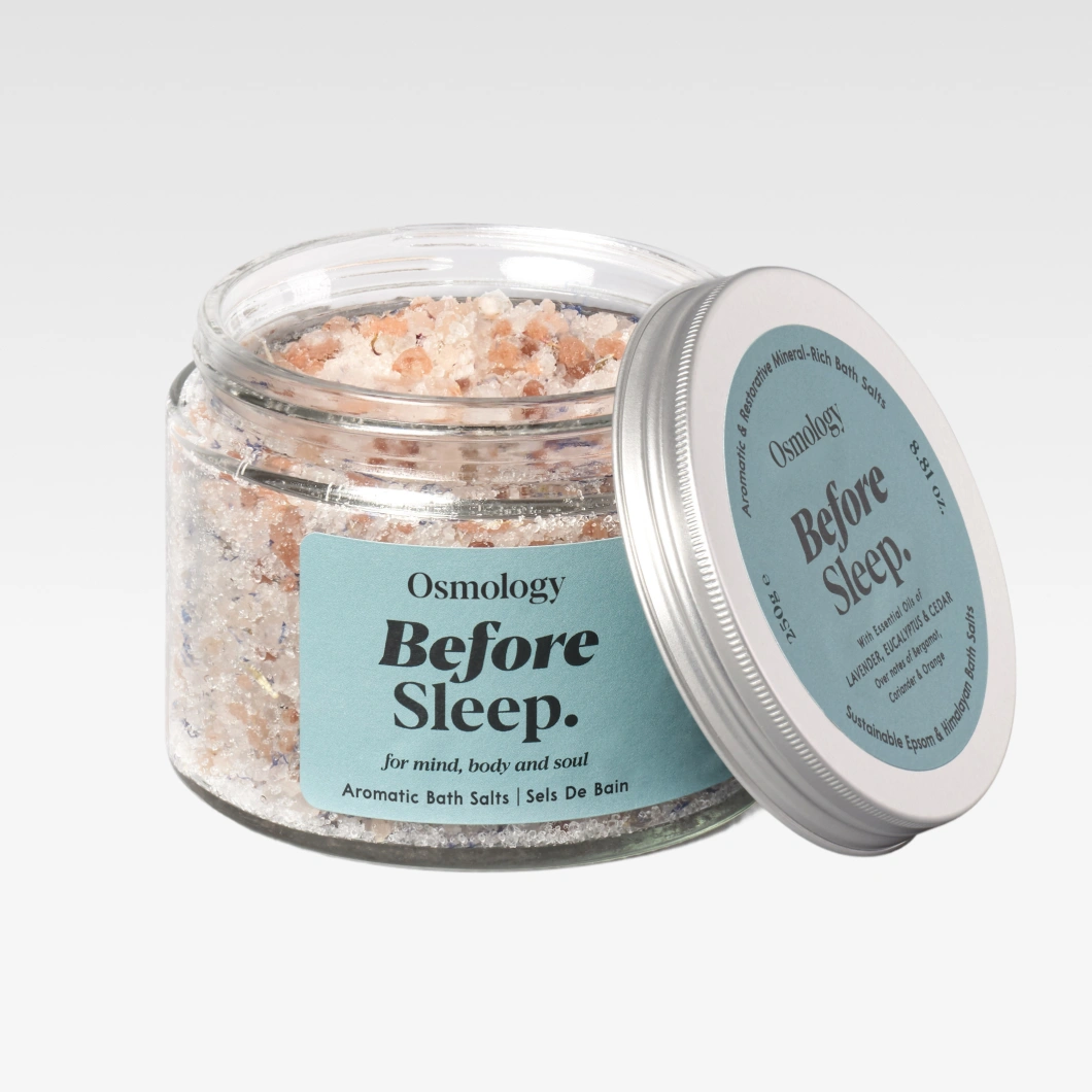 Glasburk med Osmology Before Sleep Aromatic Bath Salts fylld med rosa och vita badsaltkristaller. Etiketten visar texten “Before Sleep.”, “For mind, body and soul” och “Aromatic Bath Salts”.