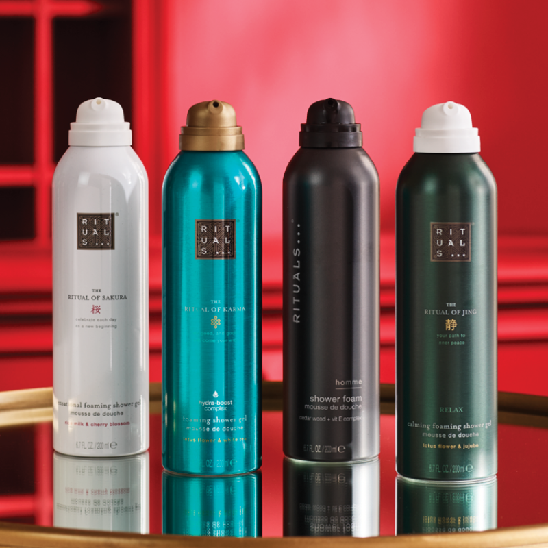 Fire Rituals dusjgeléflasker plassert ved siden av hverandre foran en rød bakgrunn. Flaskene har fargene hvit, turkis, svart og mørkegrønn.