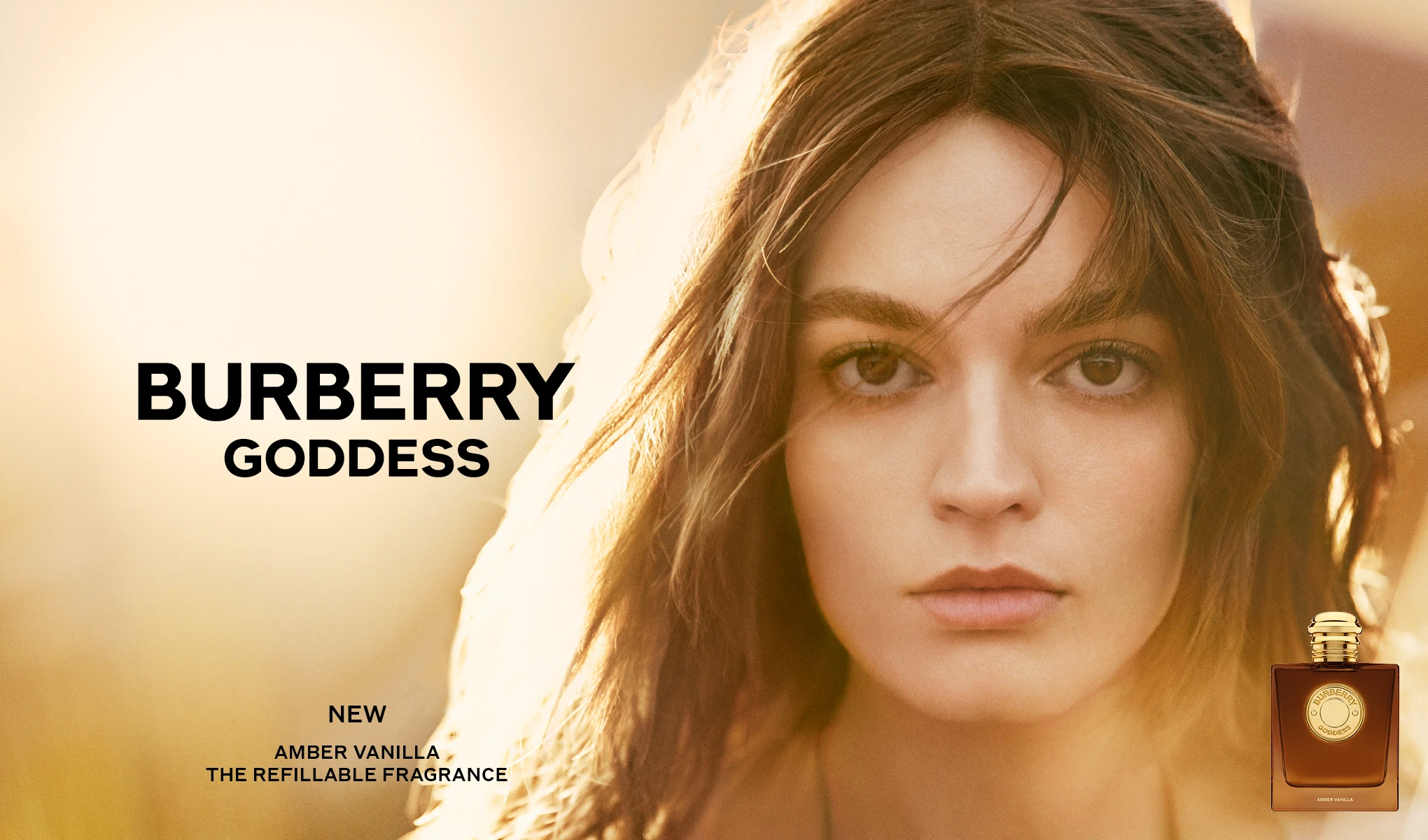Pitkähiuksinen henkilö lämpimästi valaistua taustaa vasten ja Burberry Goddess Amber Vanilla -hajuvesipullo oikeassa alakulmassa. Kuvassa näkyvät tekstit ”BURBERRY GODDESS”, ”NEW”, ”AMBER VANILLA” ja ”THE REFILLABLE FRAGRANCE”.