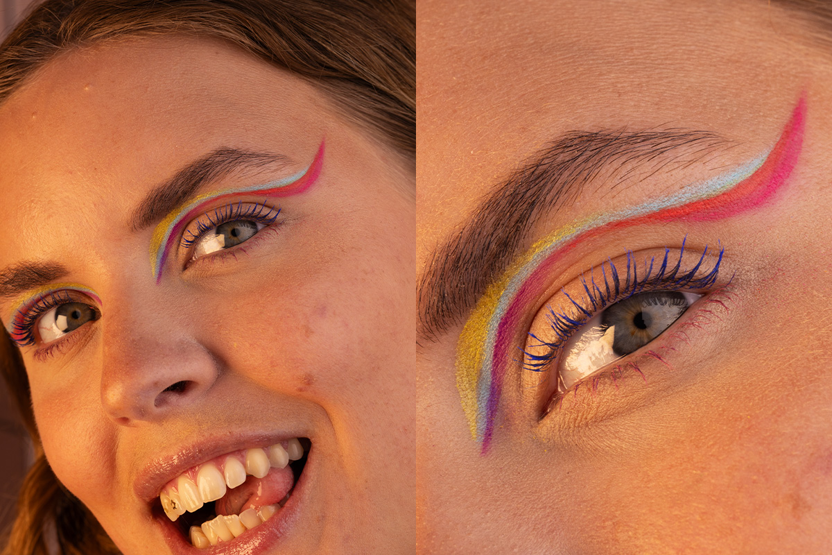 Glad person med färgglad Pride-inspirerad eyeliner i rött, blått, gult och lila samt blå mascara