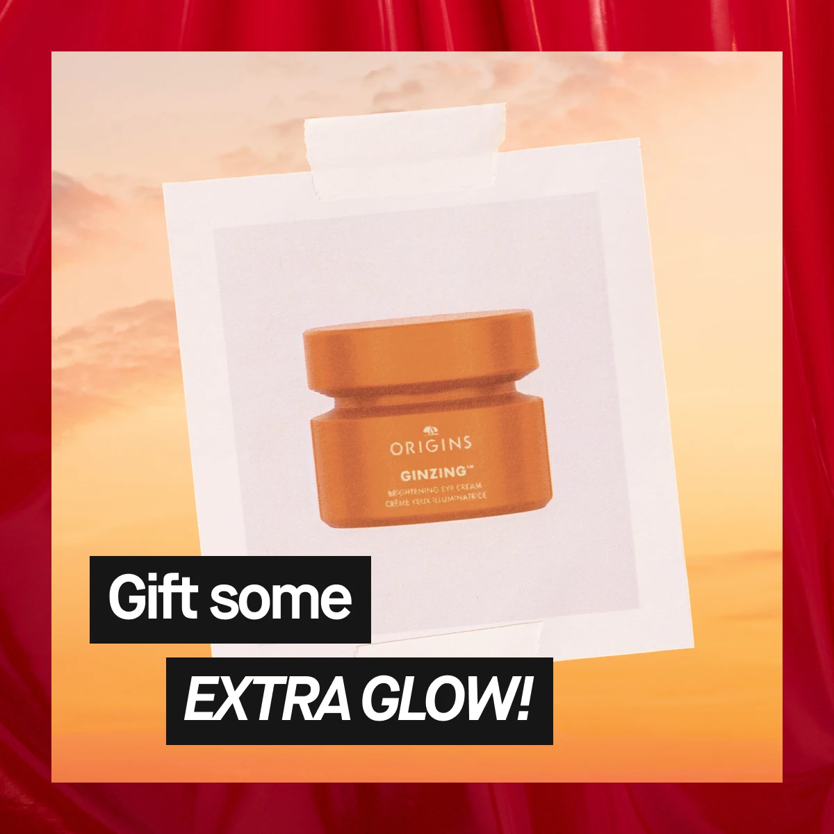 Bilde som viser en oransje boks med Origins Ginzing øyekrem. Teksten "Gift some EXTTRA GLOW" er synlig. Bakgrunnen er beige med røde detaljer.