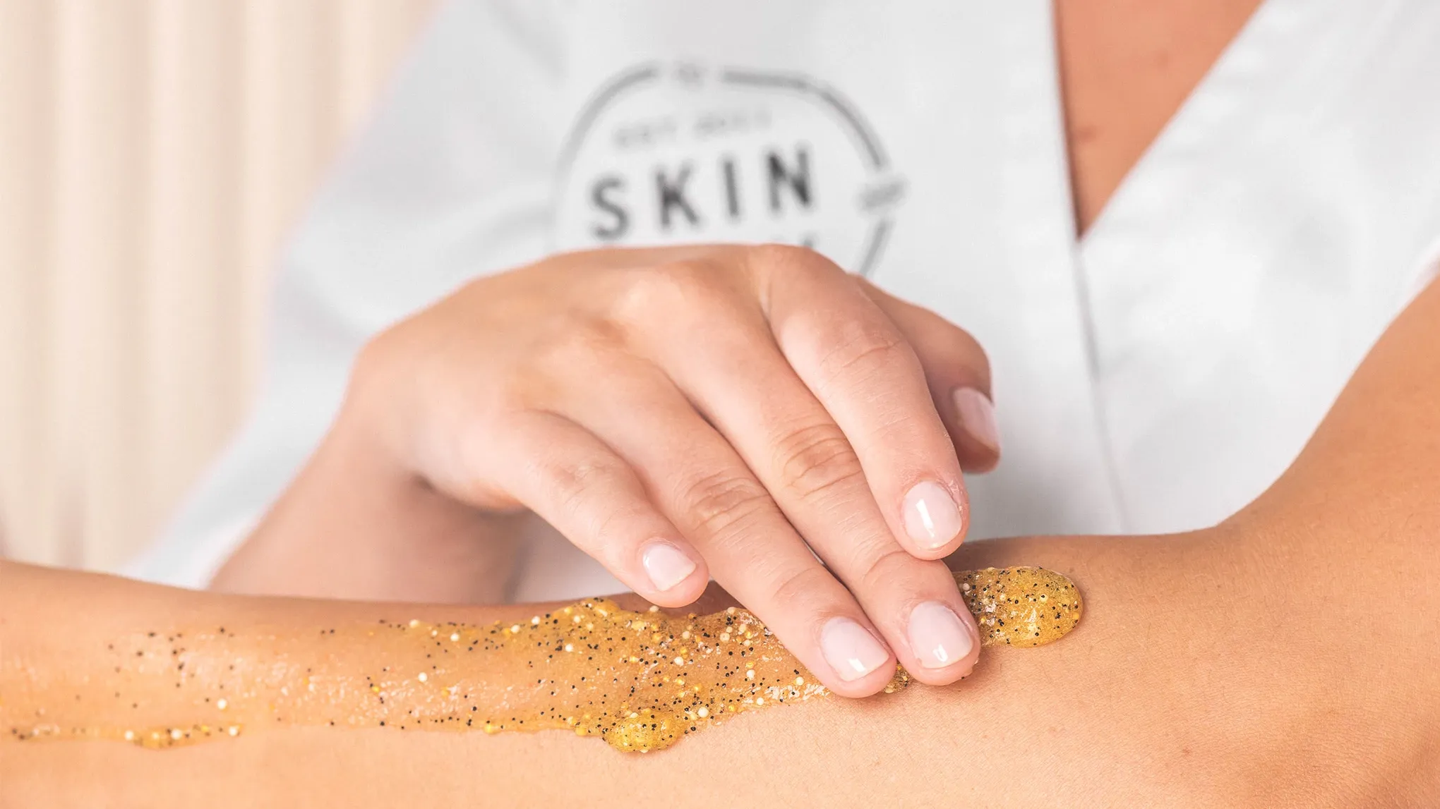 En person applicerar en gyllene skrubb på sin arm.