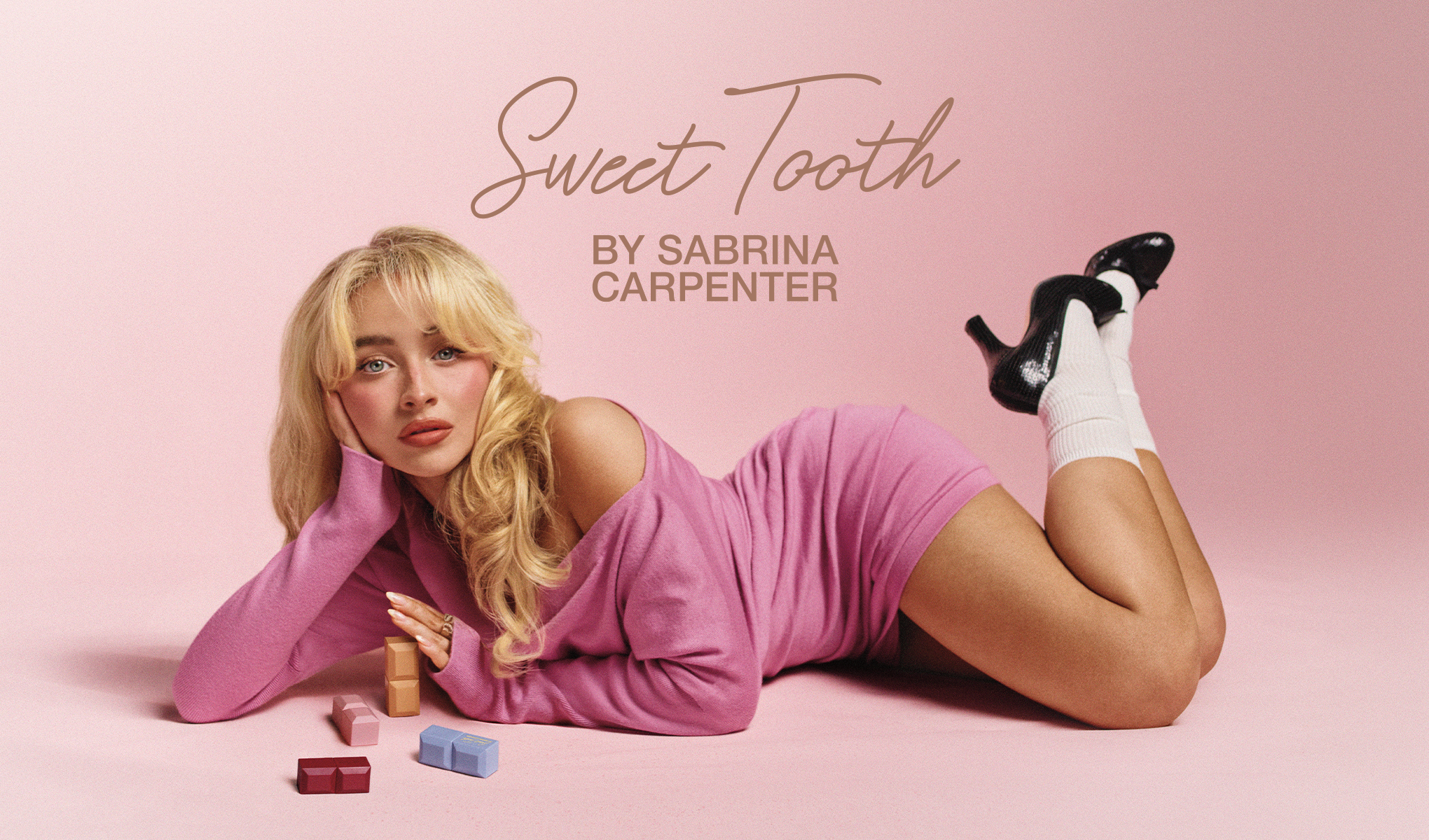 Nuori nainen makaa vaaleanpunaisella taustalla, yllään pinkki mekko, ympärillään värikkäitä tuotteita.