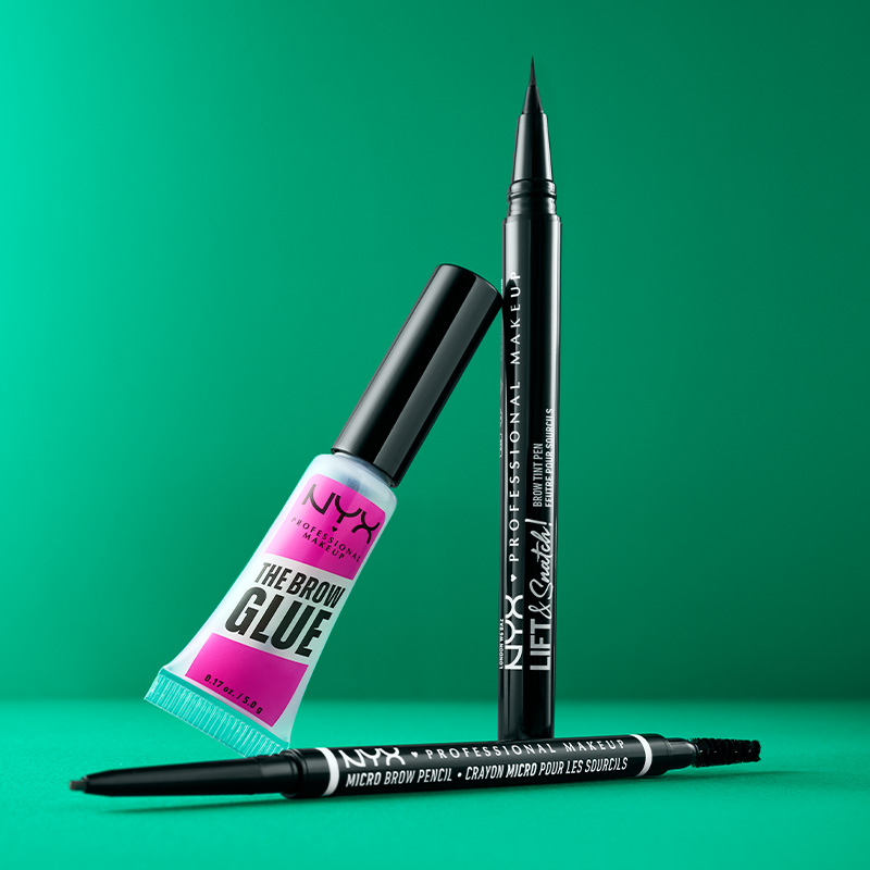 Kolme NYX Professional Makeup -tuotetta vihreää taustaa vasten. Tuotteet ovat vaaleanpunainen ja sininen tuubi, musta luomivärikynä ja musta kulmakynä.