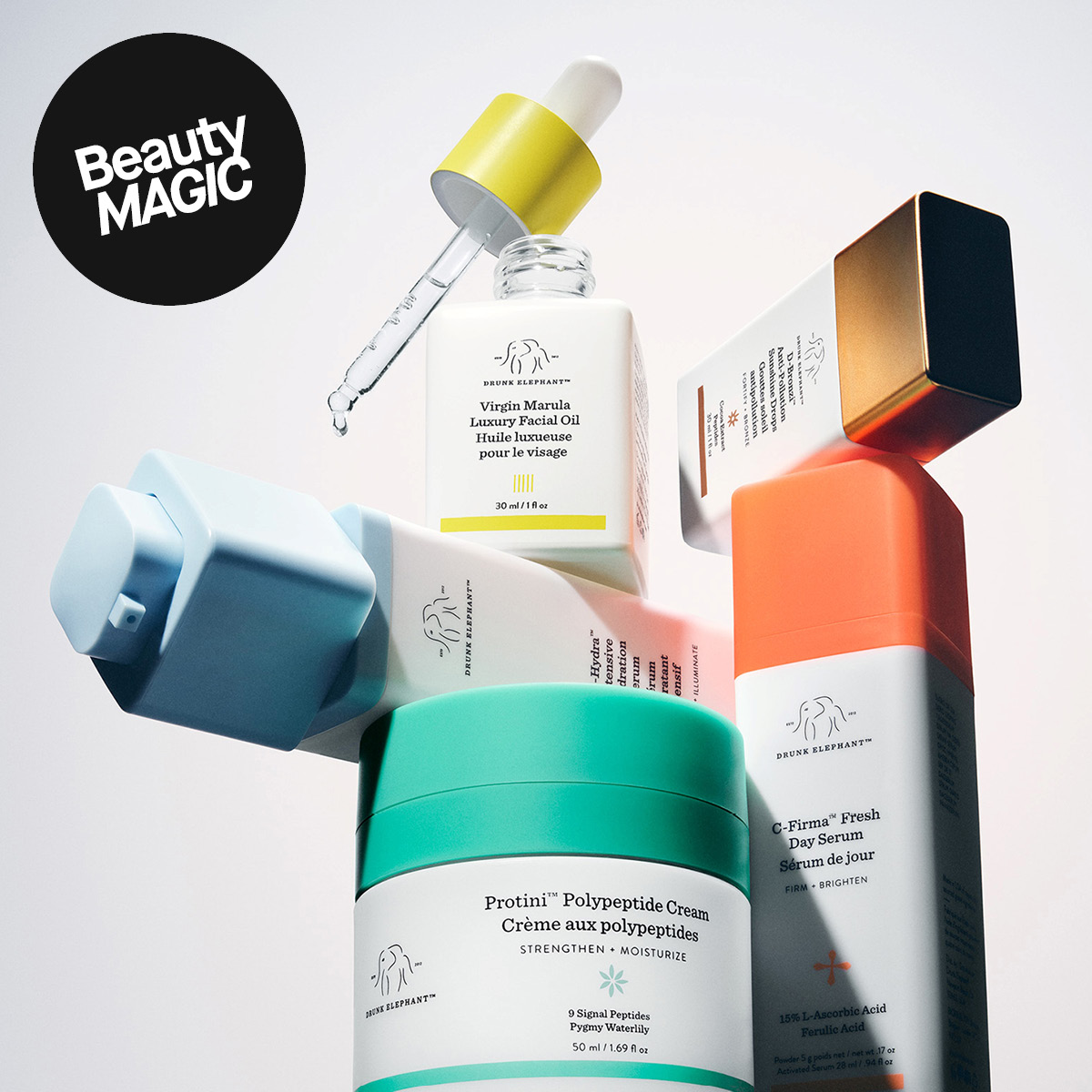 Drunk Elephant -ihonhoitotuotteita vaaleaa taustaa vasten, mukana seerumi, kasvoöljy ja kasvovoide. Kuvassa näkyy tekstit “Beauty MAGIC!”, Virgin Marula Luxury Facial Oil, Protini Polypeptide Cream ja C-Firma Fresh Day Serum sekä turkoosit, oranssit, keltaiset ja siniset pakkaukset.