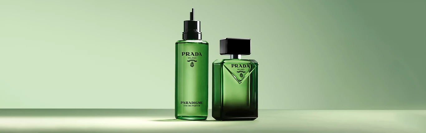Två gröna Prada Paradigme-parfymflaskor på en ljusgrön bakgrund.