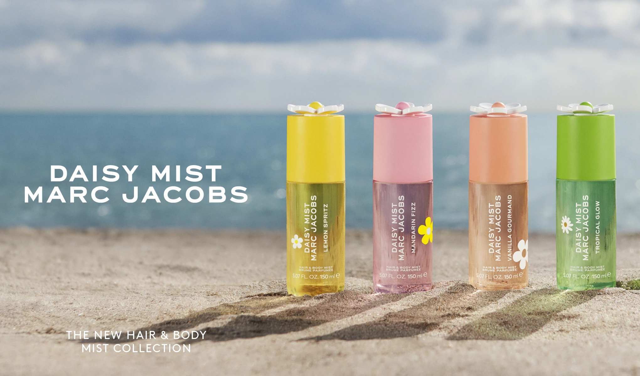 Fire Marc Jacobs Daisy Mist Hair & Body Mist står på sand foran havet. Synlig tekst: "DAISY MIST MARC JACOBS" og "THE NEW HAIR & BODY MIST COLLECTION". Produktene er Lemon Spritz, Mandarin Fizz, Vanilla Gourmand og Tropical Glow med blomsterformede korker og synlig produkttekst.